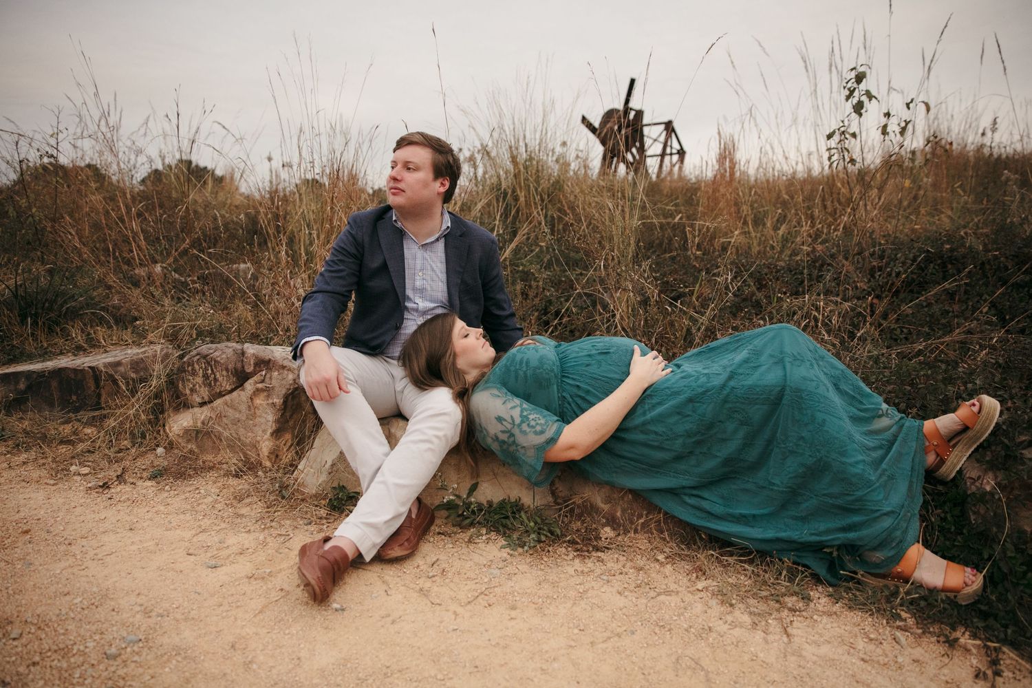 Romantic couple posing in scenic golden field at sunset with natural foliage in background.