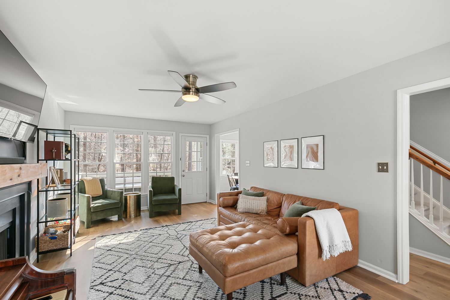 Bright living room with brown leather tufted chaise, green chairs, fireplace, ceiling fan, and hardwood floors.