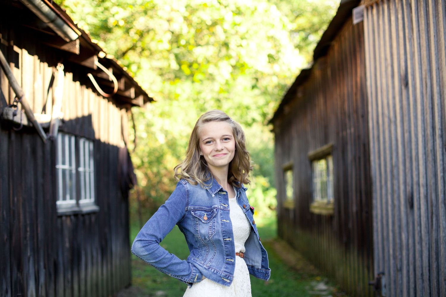 A portrait between wooden barn buildings on a sunny day.