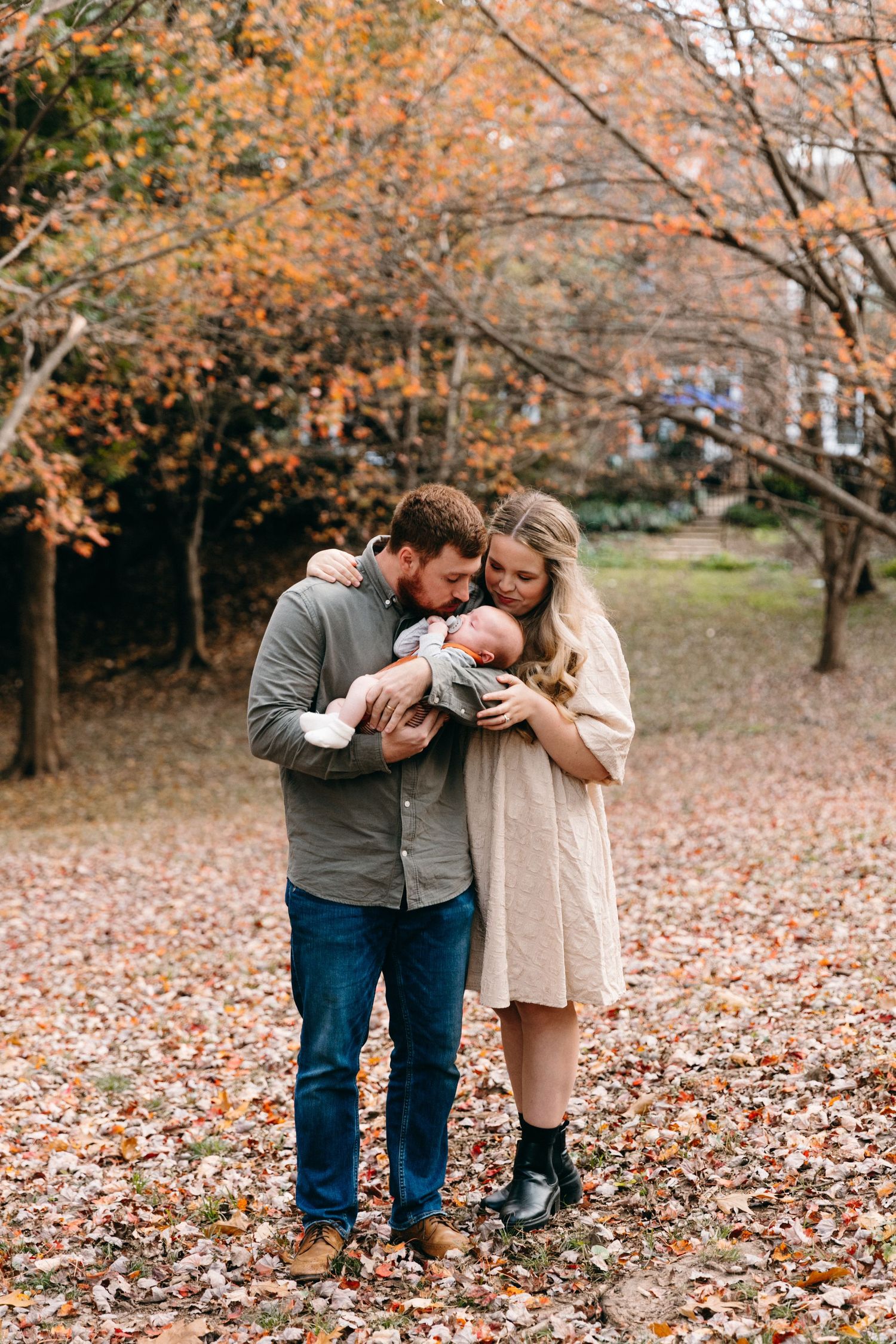 Couple holding baby together among fall foliage.