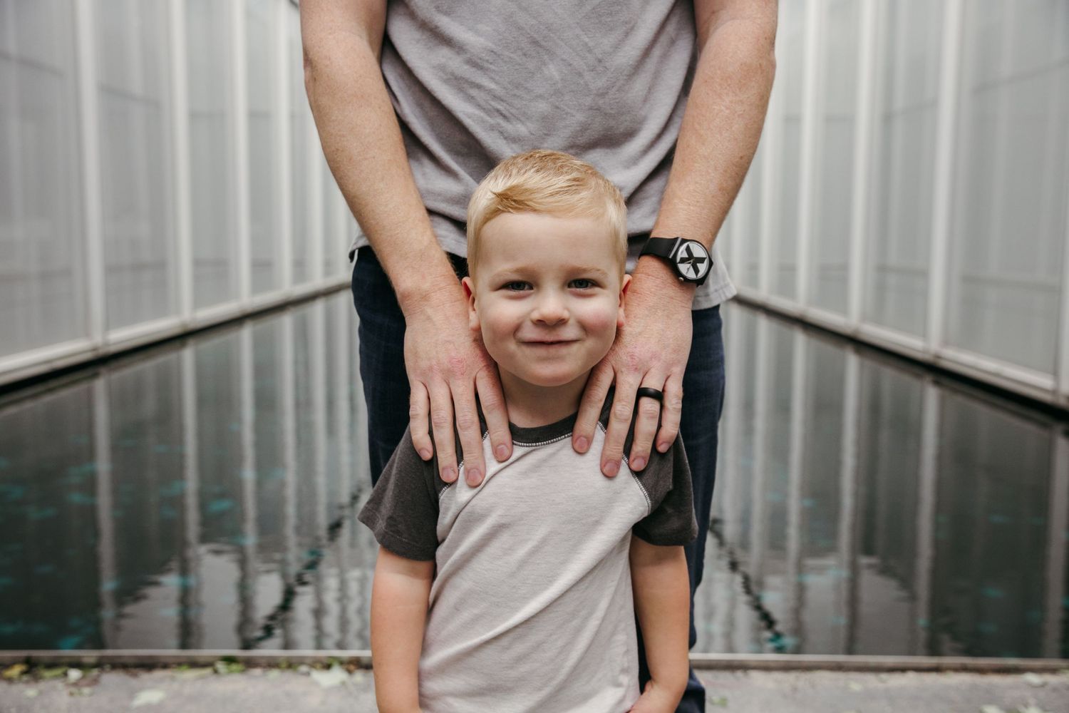 Parent placing hands on young child's shoulders in a long reflective corridor.