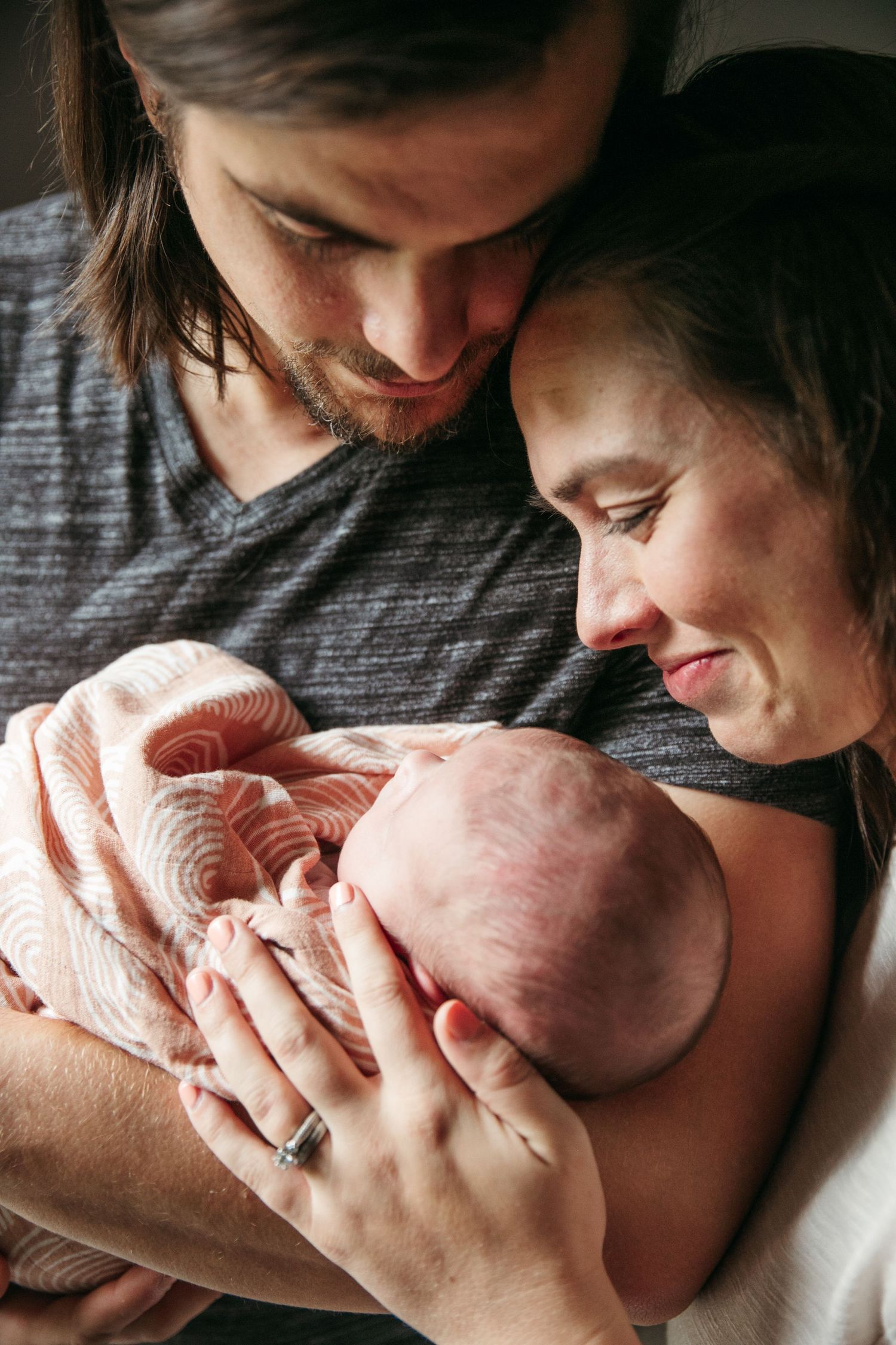New parents lovingly gaze at their newborn baby wrapped in a pink blanket.