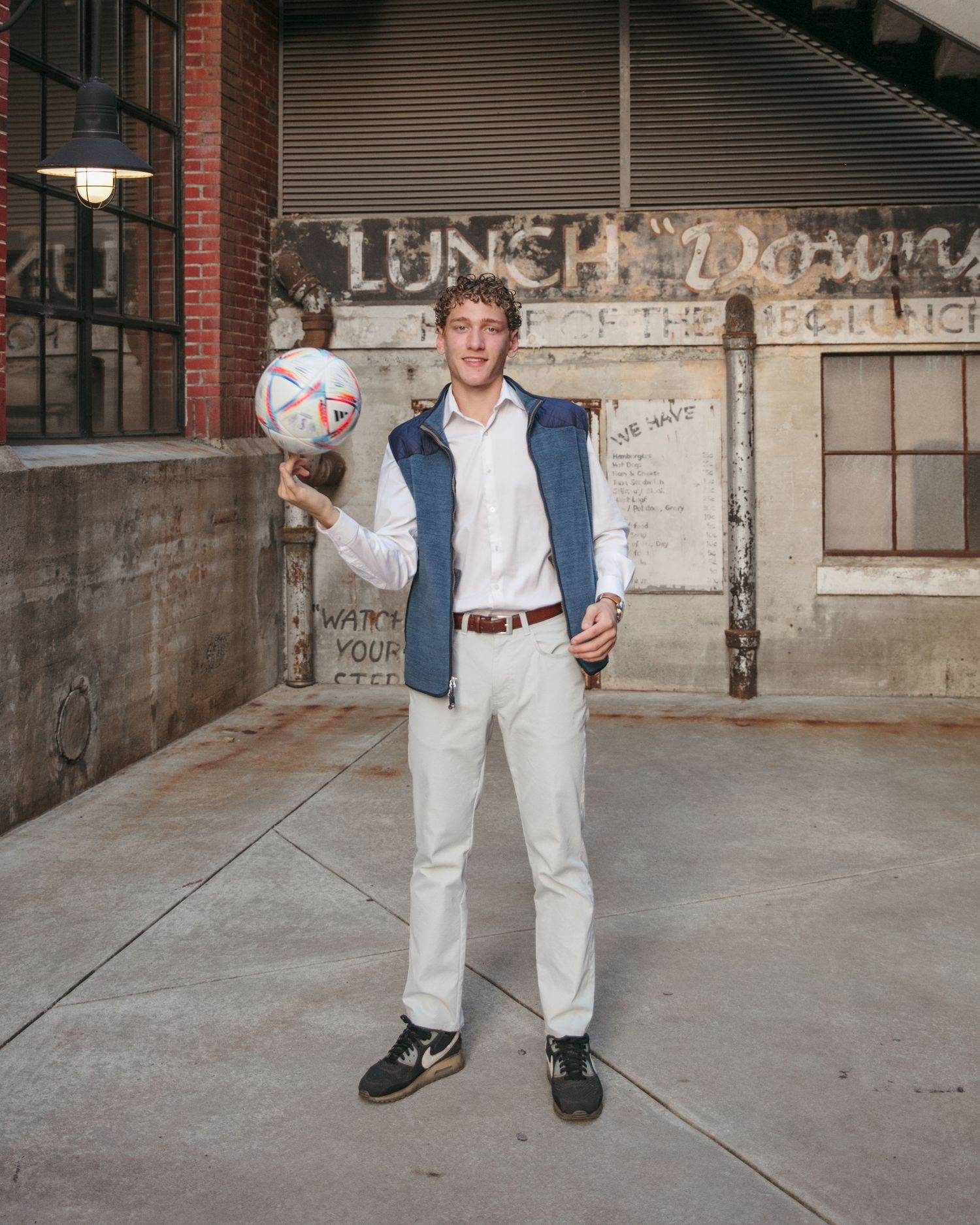 Person in casual attire holding soccer ball against graffiti wall.