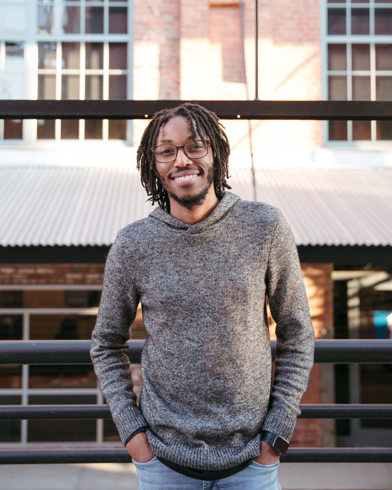 Person in knit sweater standing against urban backdrop with windows.