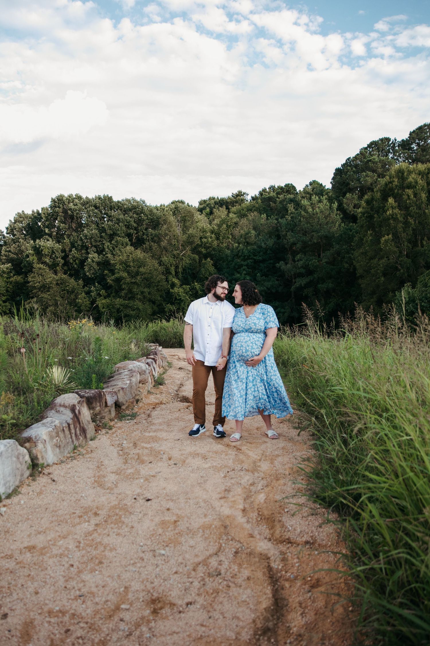 Two people walking together on a scenic dirt trail bordered by greenery and trees.