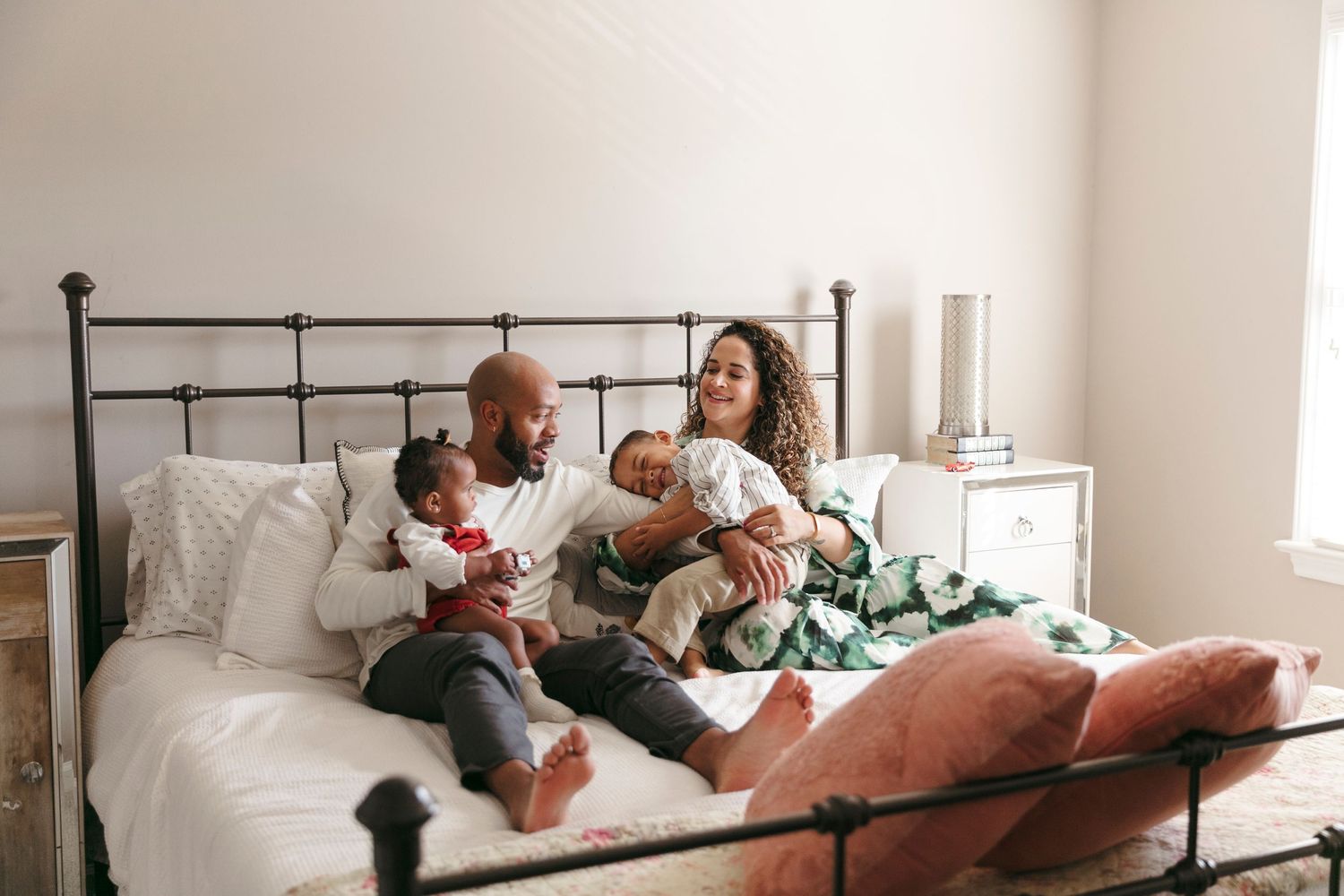 Happy family relaxing together on white bedding while looking at phone.