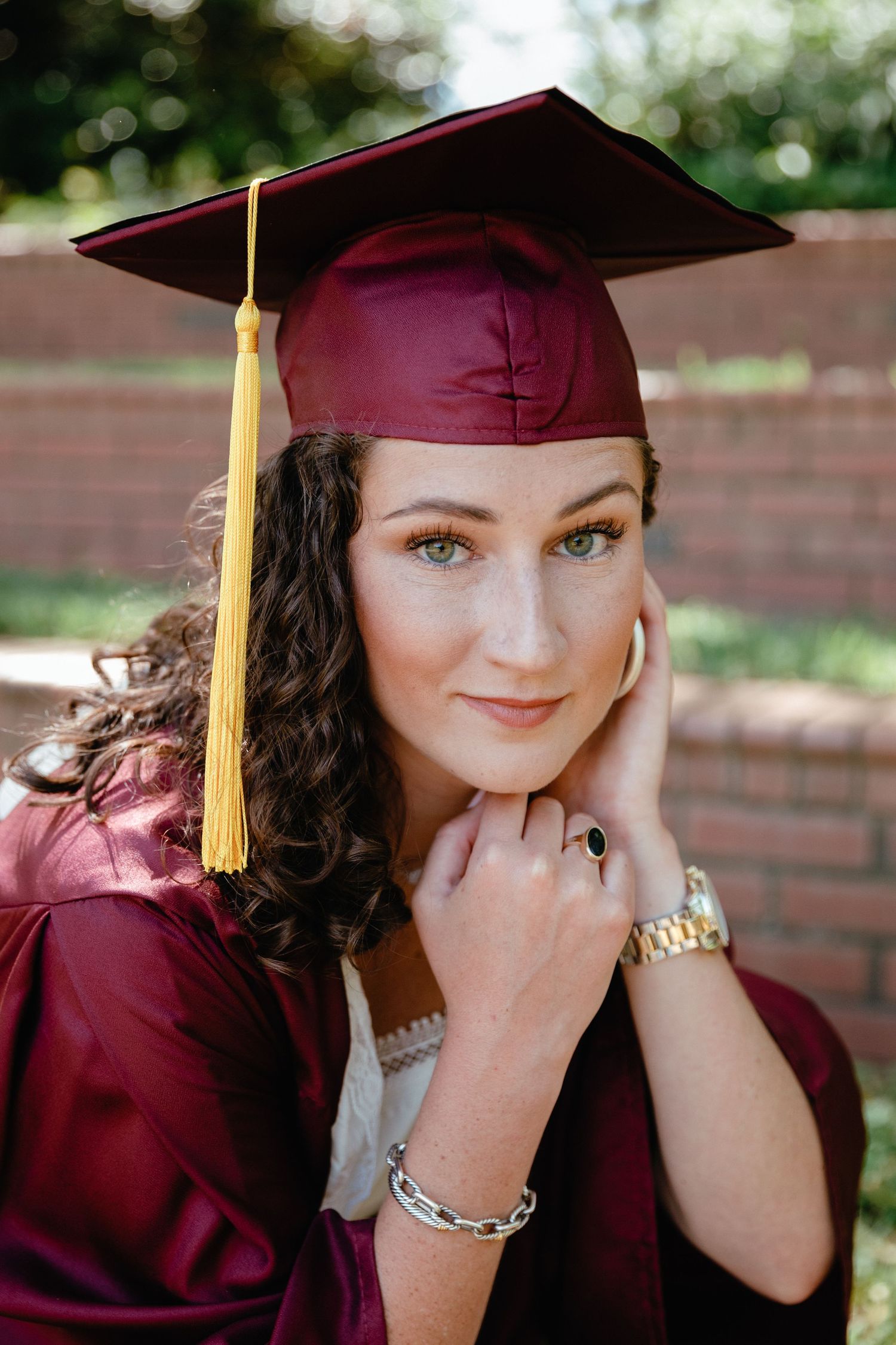 Graduate in maroon cap and gown poses for close-up photos outdoors.
