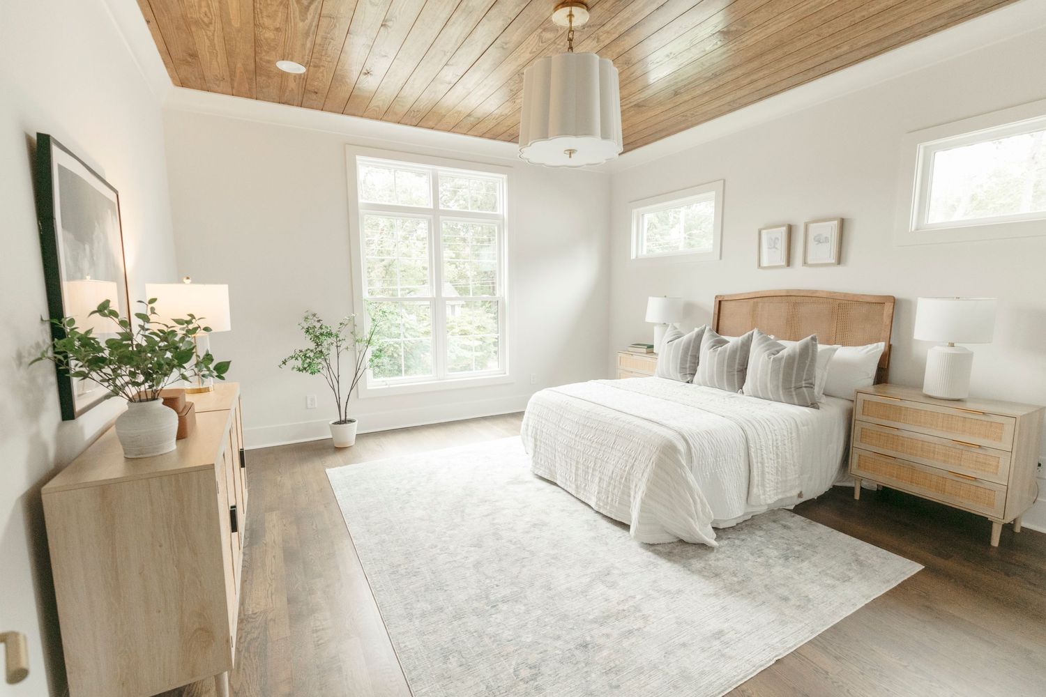 Serene bedroom featuring wood plank ceiling, white bedding, and natural light from multiple windows.