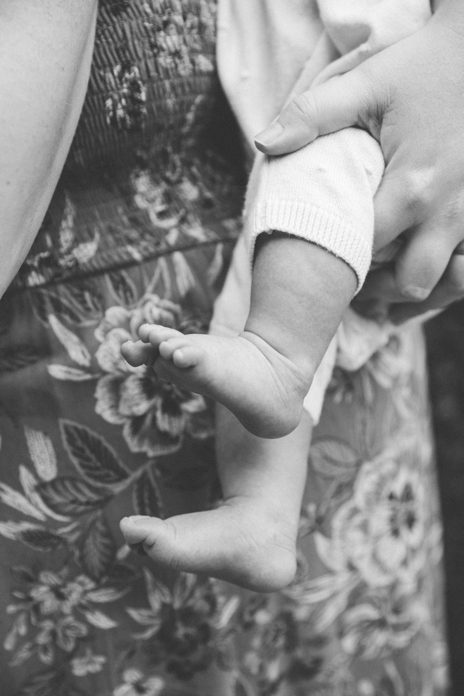 A series of black and white photos showing a hand gently holding and caressing a foot against a floral background.