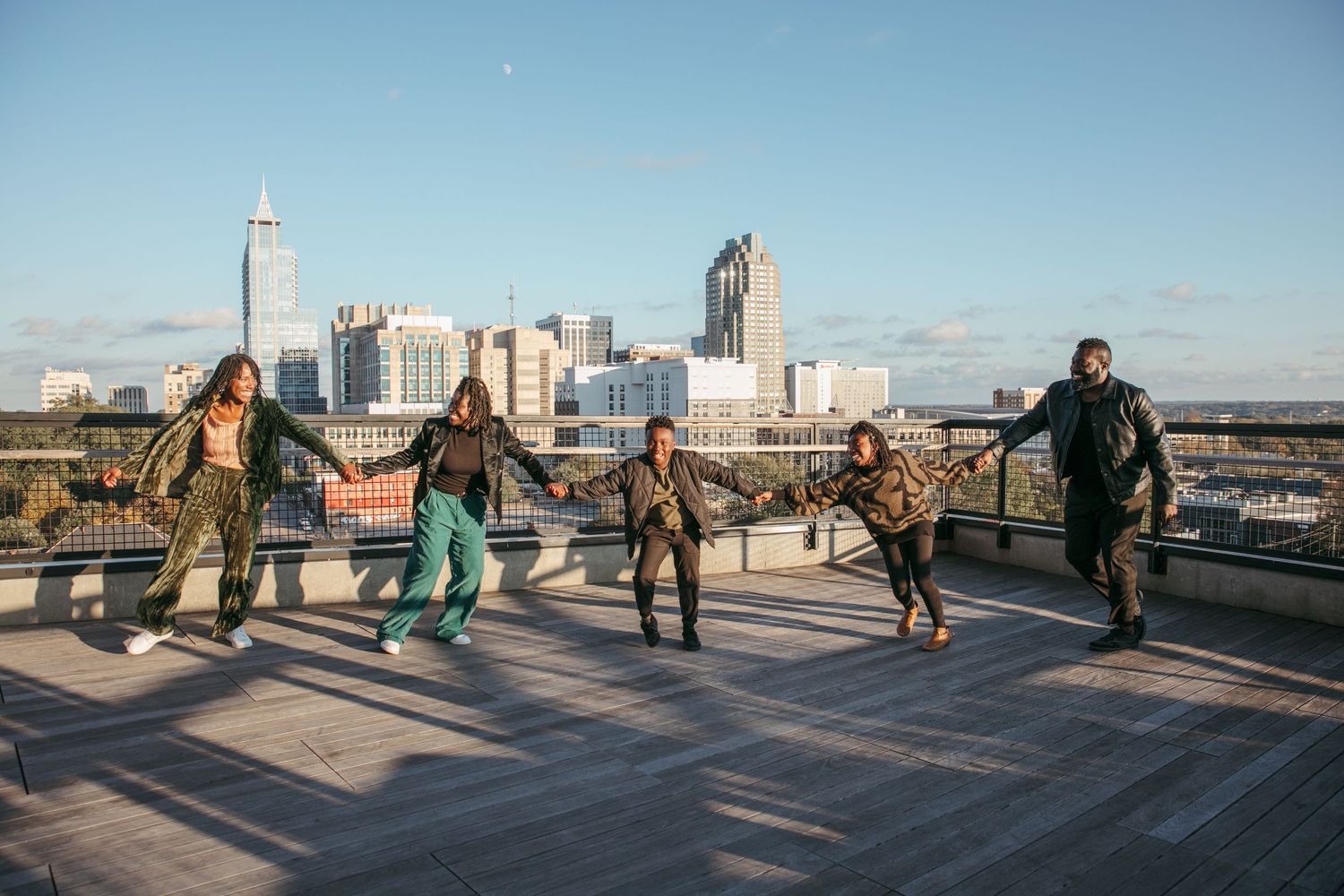 Group of friends running and jumping on rooftop with city skyline in background.