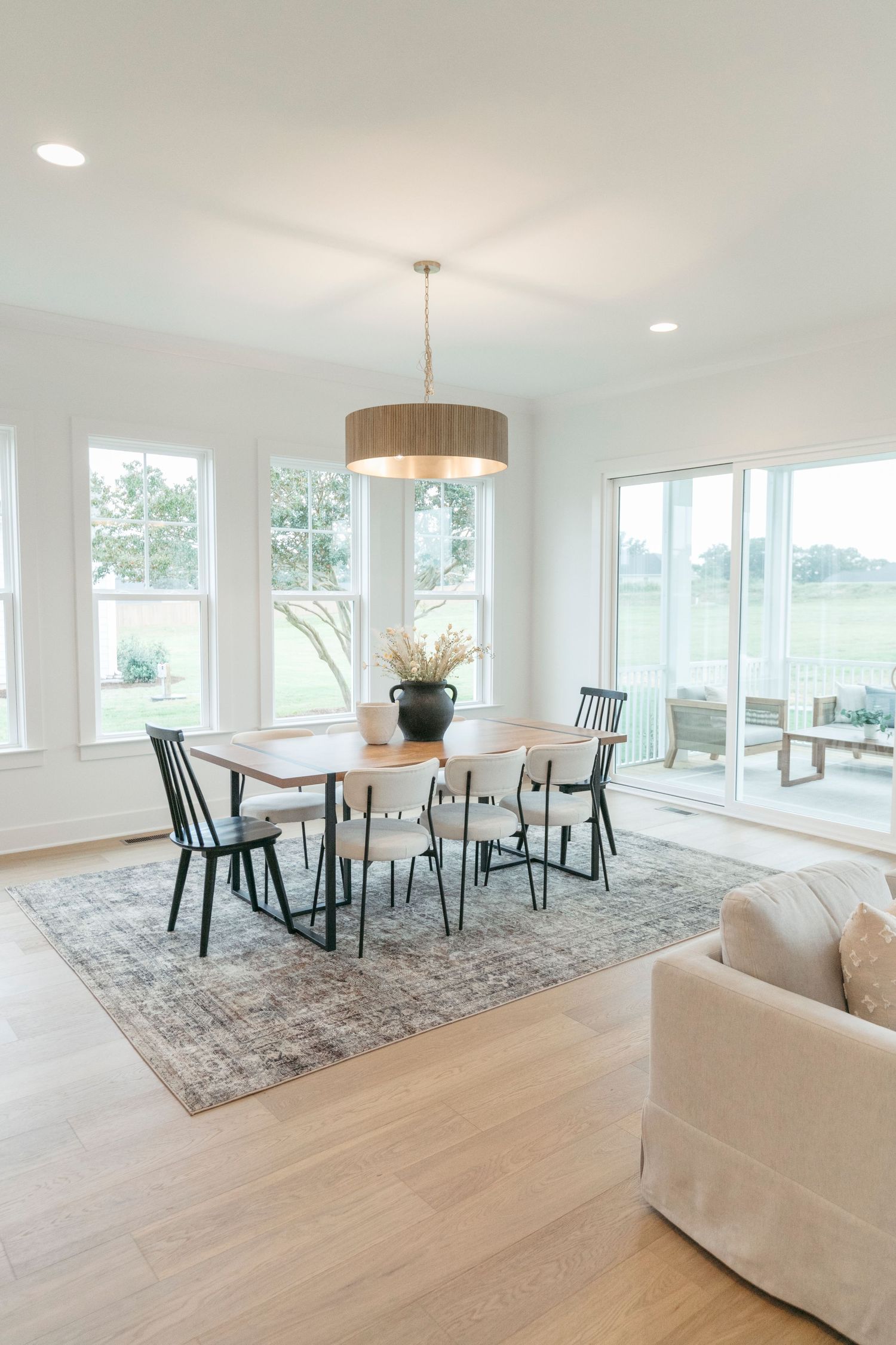 Bright dining area with round table, black chairs and drum pendant light overlooking coastal views.