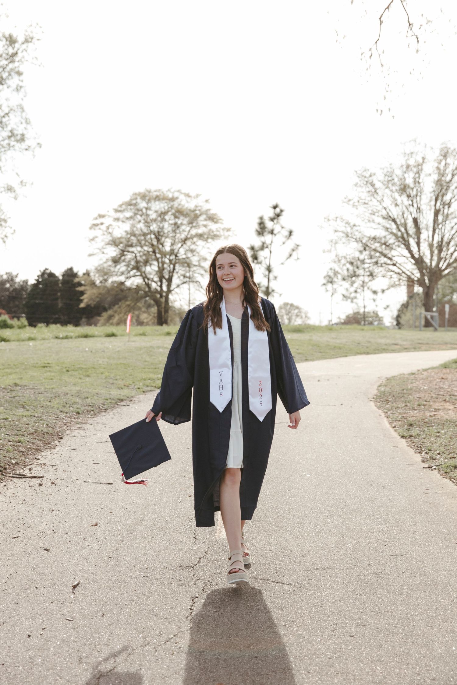 Graduate in blue cap and gown walking along a curved path during outdoor graduation photoshoot.