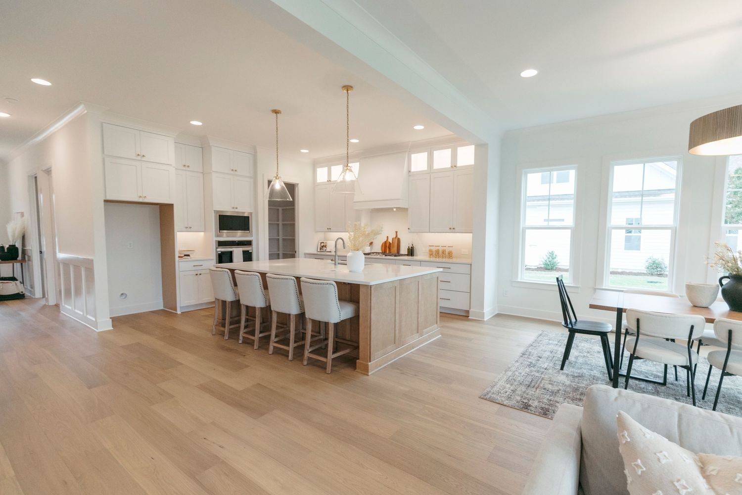 Open concept kitchen with white cabinets, island seating and light hardwood floors.