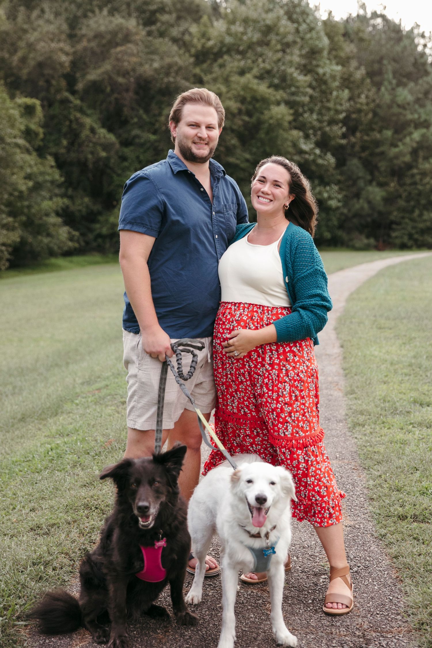 Couple with two dogs posing together on a trail surrounded by greenery.