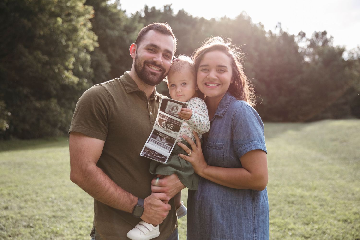 Couple holding ultrasound photos in a sunny field during sunset.