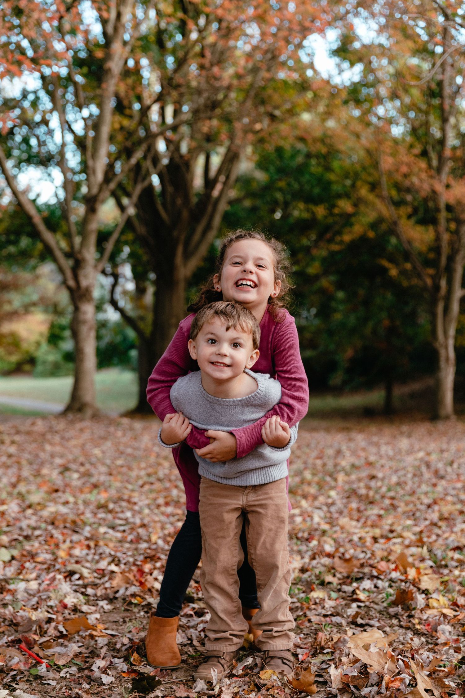 Two children playing together outdoors in autumn with fallen leaves.