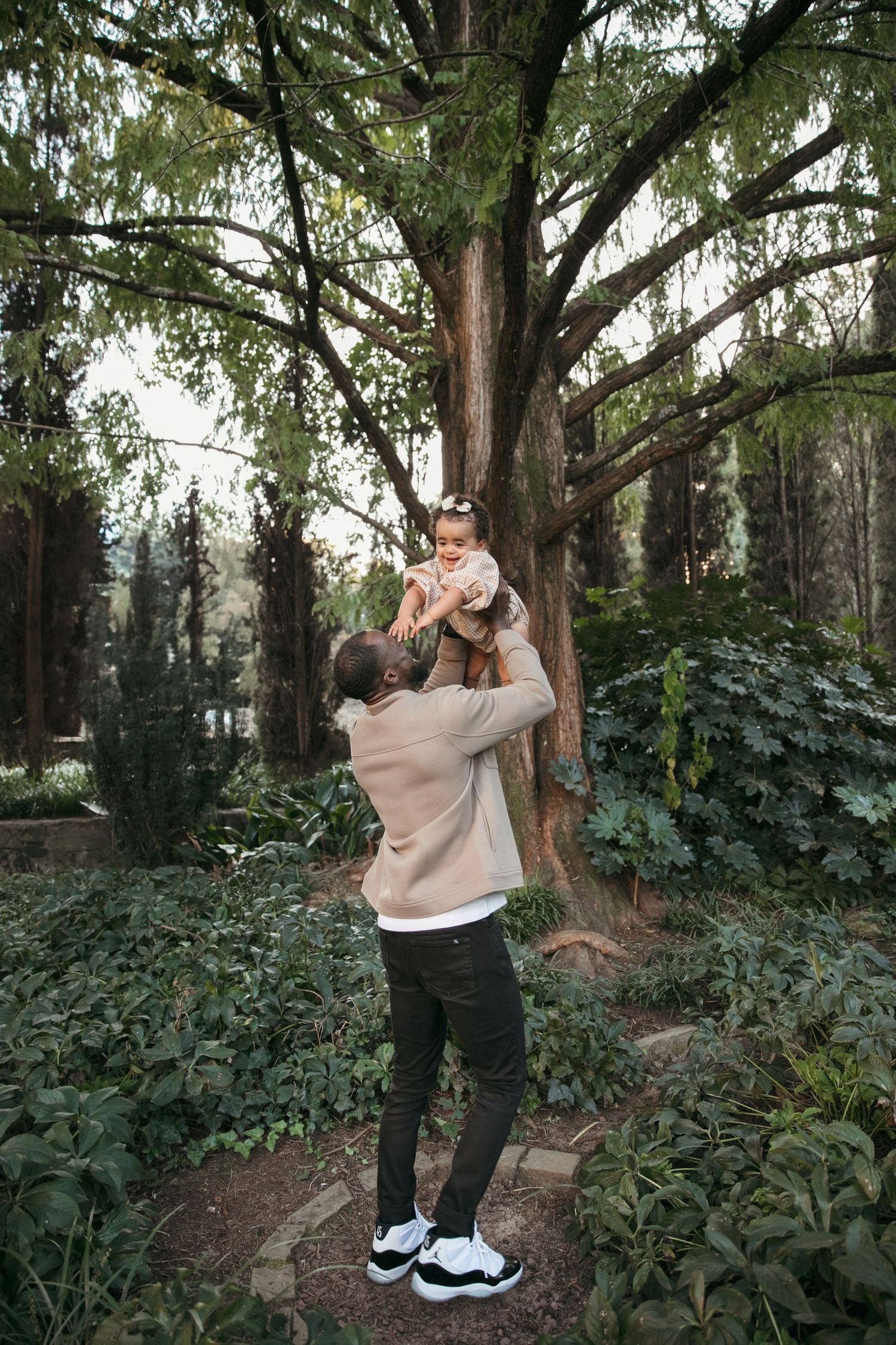 A tender moment captured beneath a large tree in a lush garden setting.