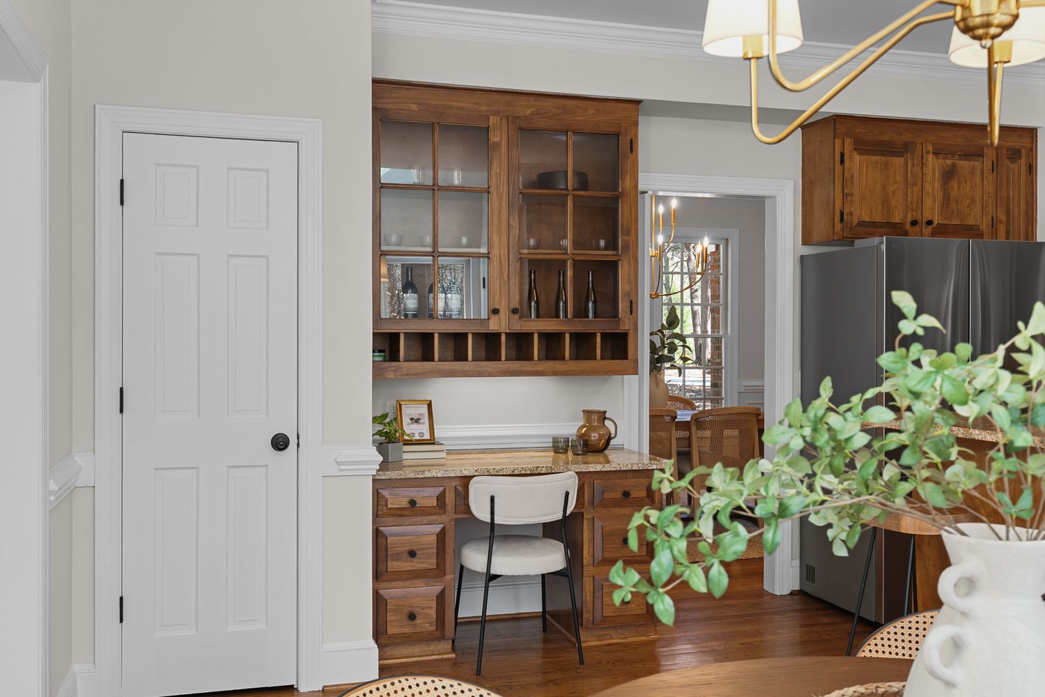 Warm wooden built-in bar cabinet with glass doors and wine rack beside stainless steel refrigerator.