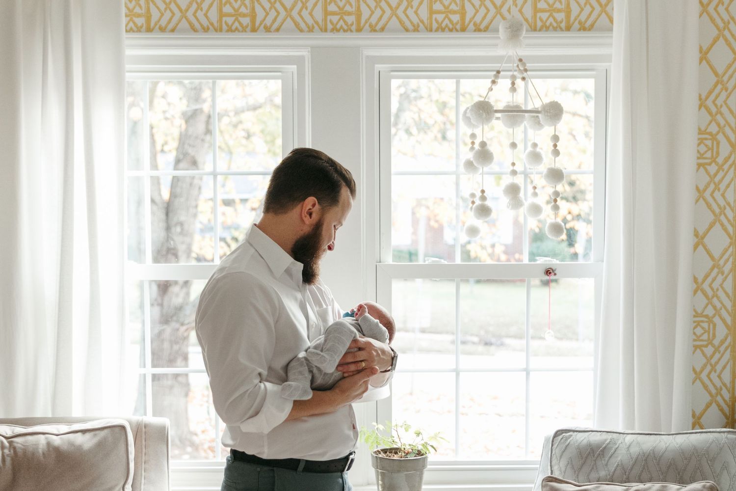 Someone in a white chef's coat stands in a bright, sunlit kitchen while looking at their phone.