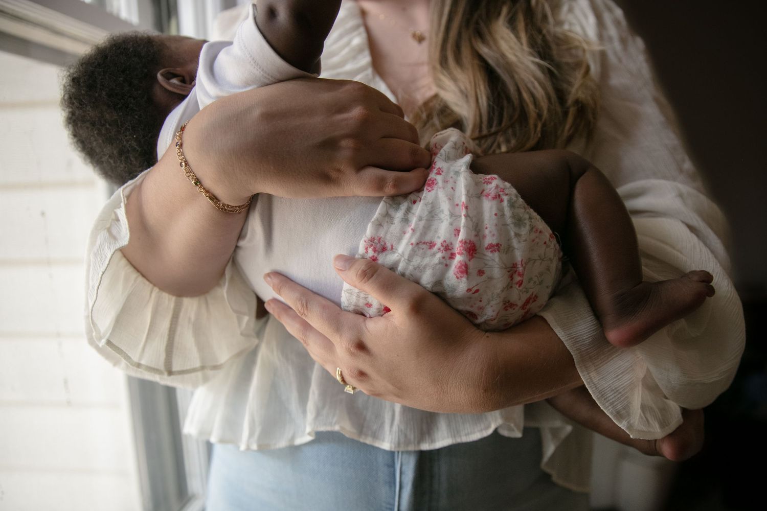 A person holds a newborn baby wrapped in floral fabric near a bright window.