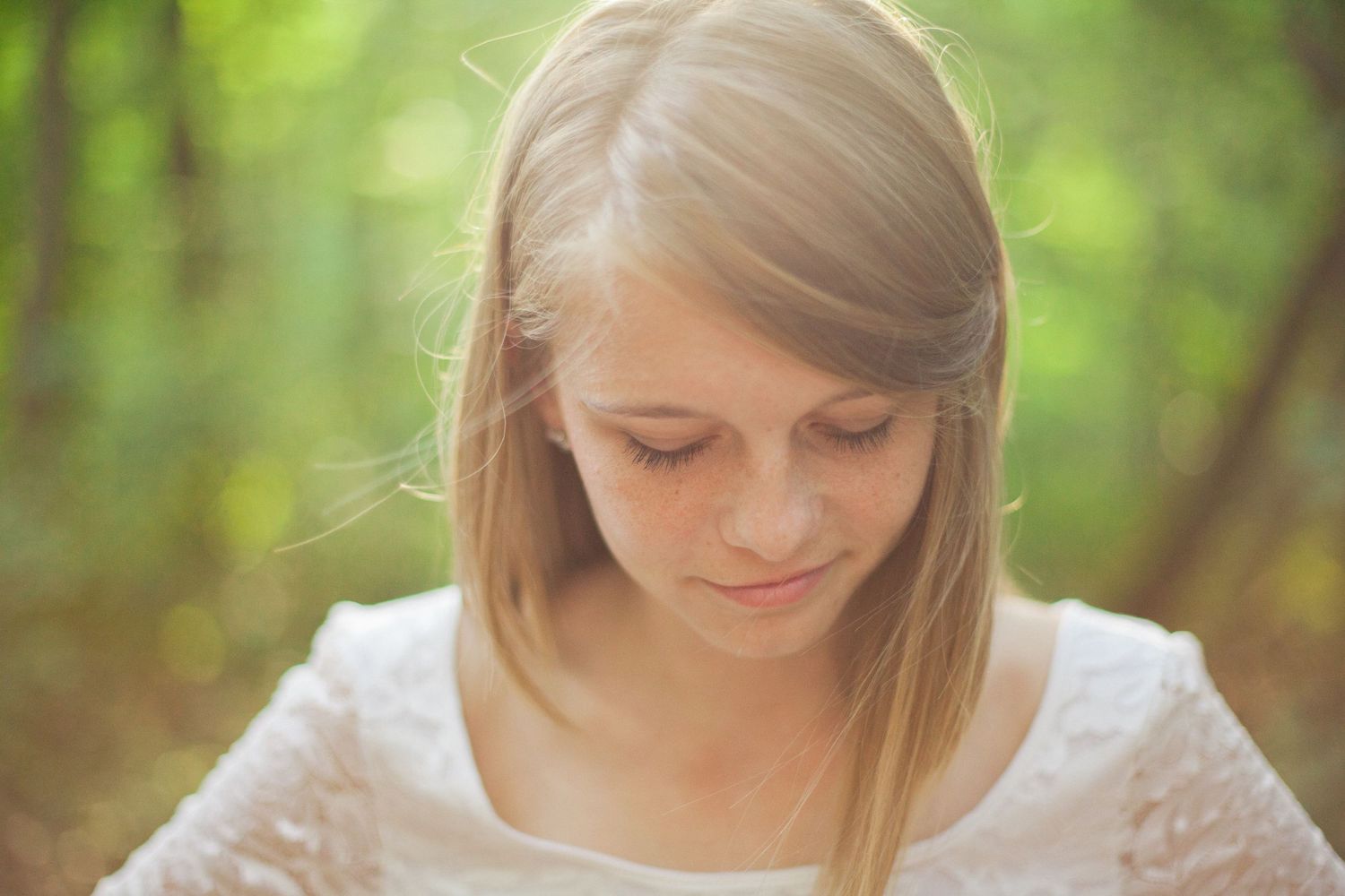 A soft portrait of someone in a white lace dress against a blurred green natural background.