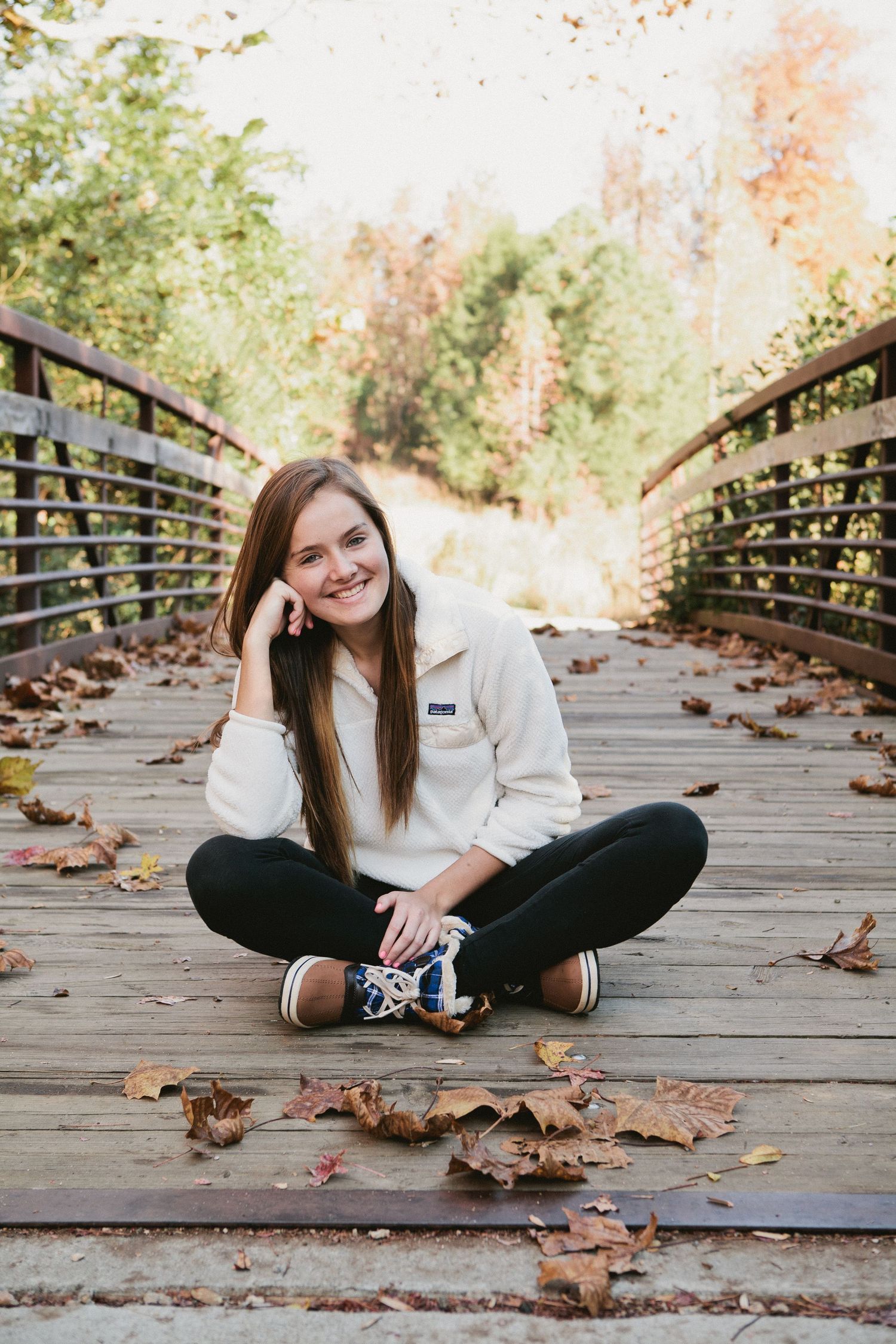 A person sits cross-legged on a wooden bridge surrounded by autumn leaves.