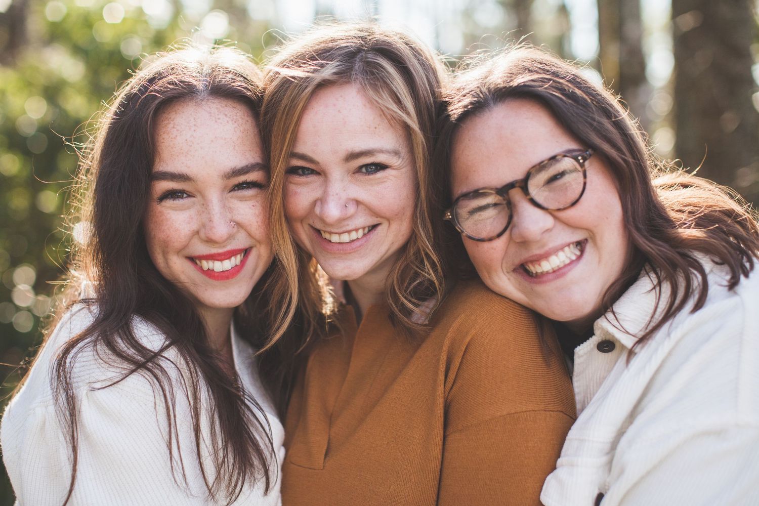 Three friends smiling together outdoors on a sunny day.
