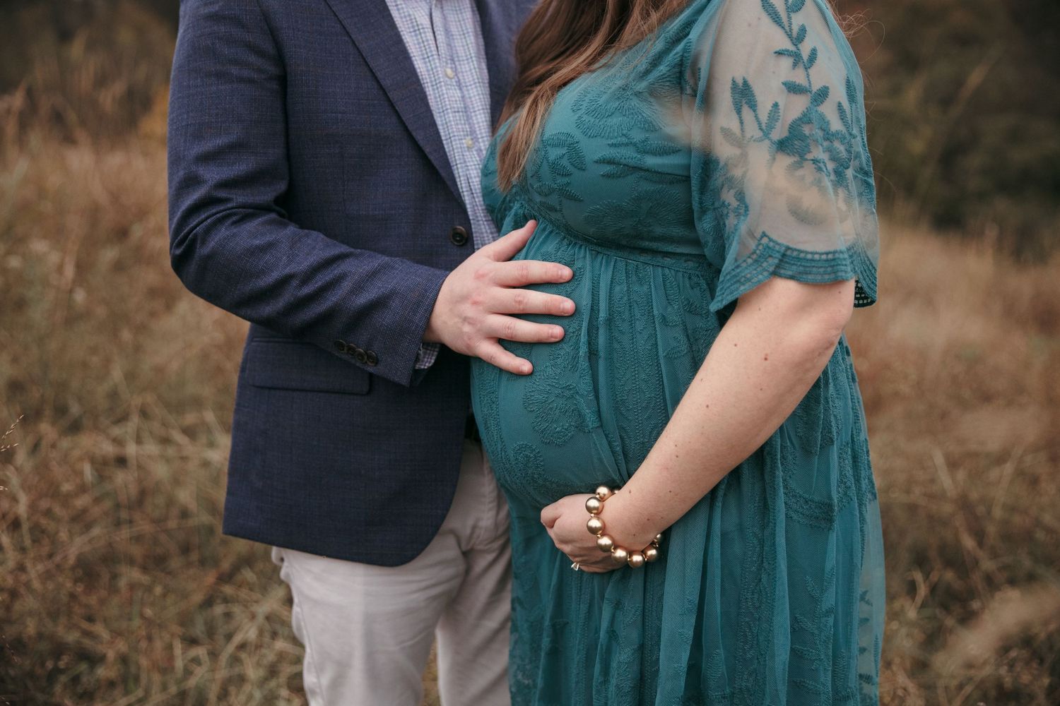 Close-up shot of maternity pose with hands on belly in autumn field.