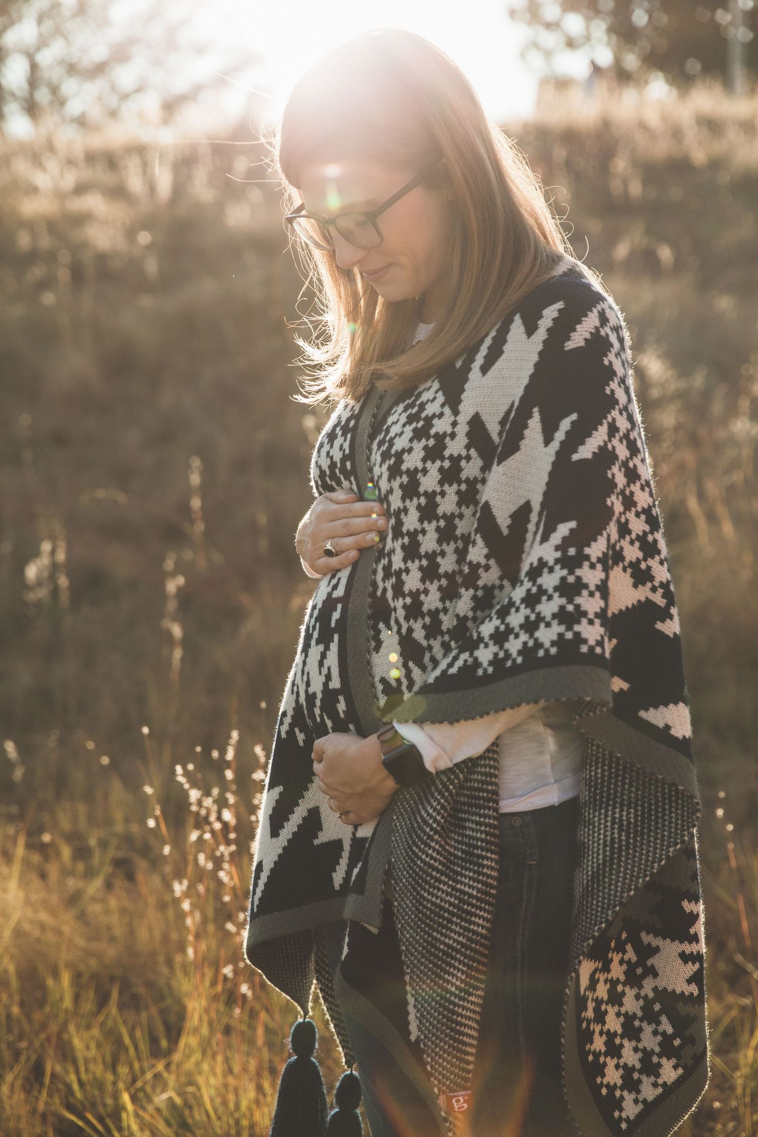 Person wearing houndstooth pattern poncho in autumn field during sunset.