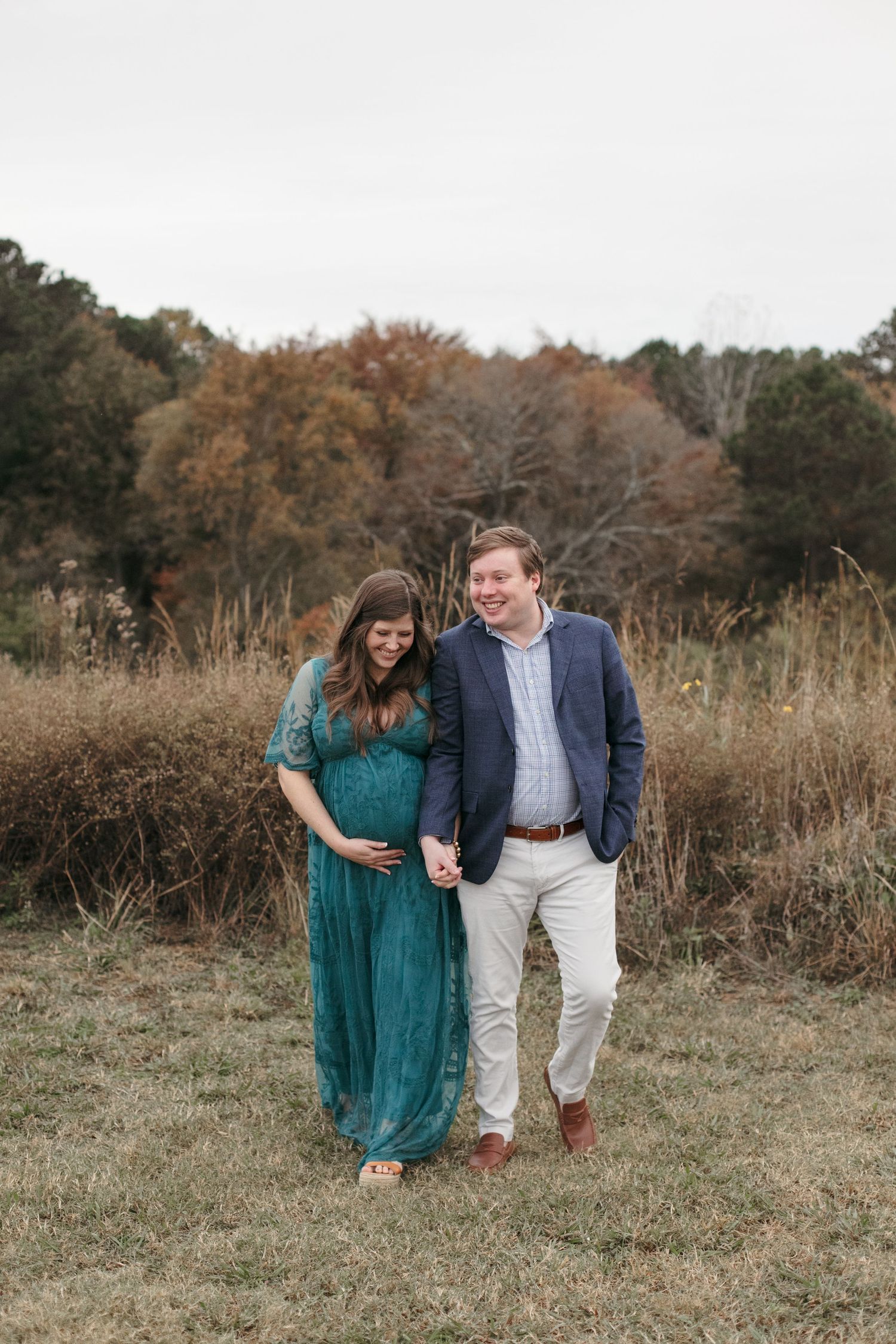 Couple walking together through autumn field in formal attire.