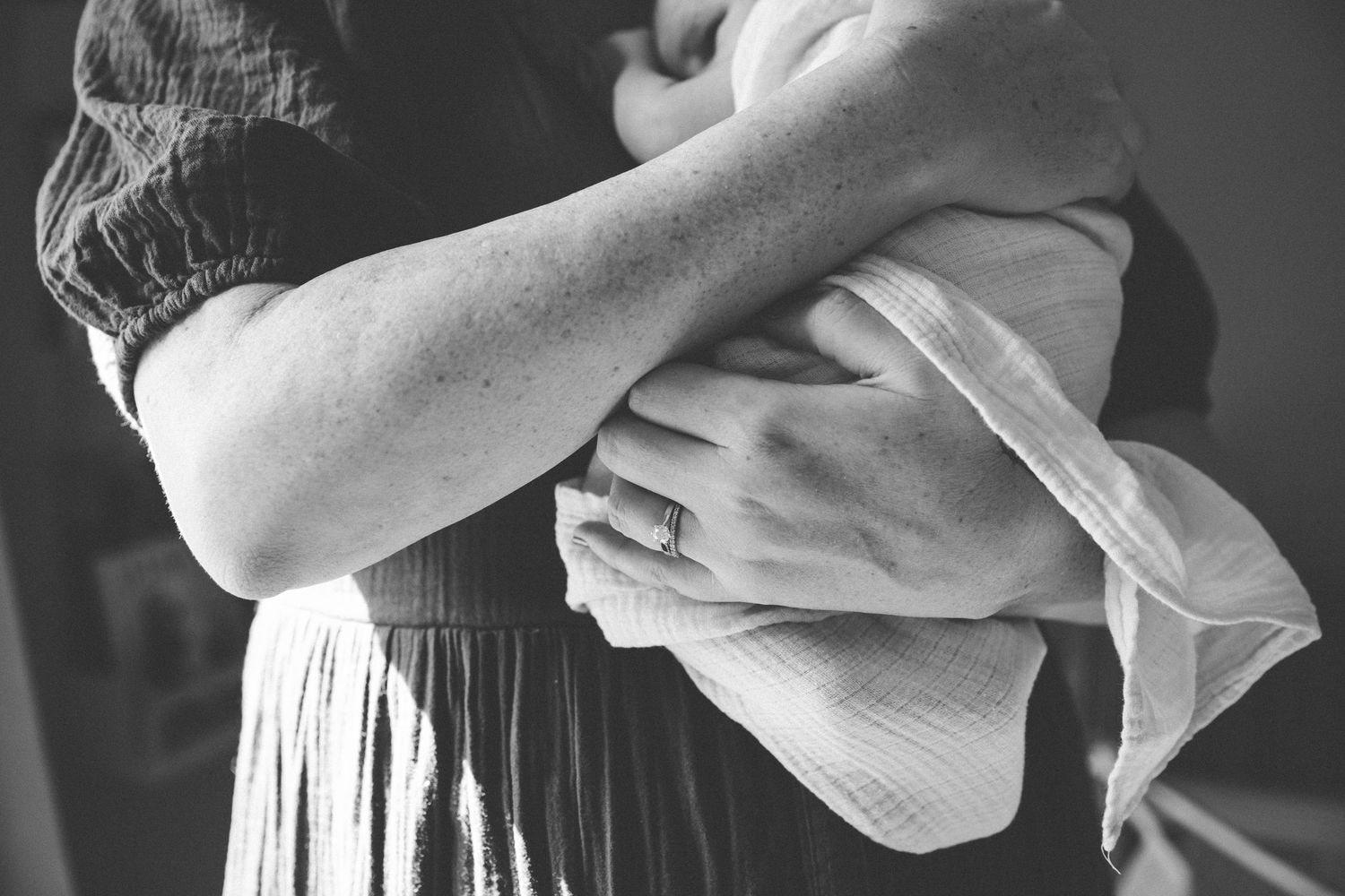 Black and white image of hands cradling a newborn wrapped in soft fabric.