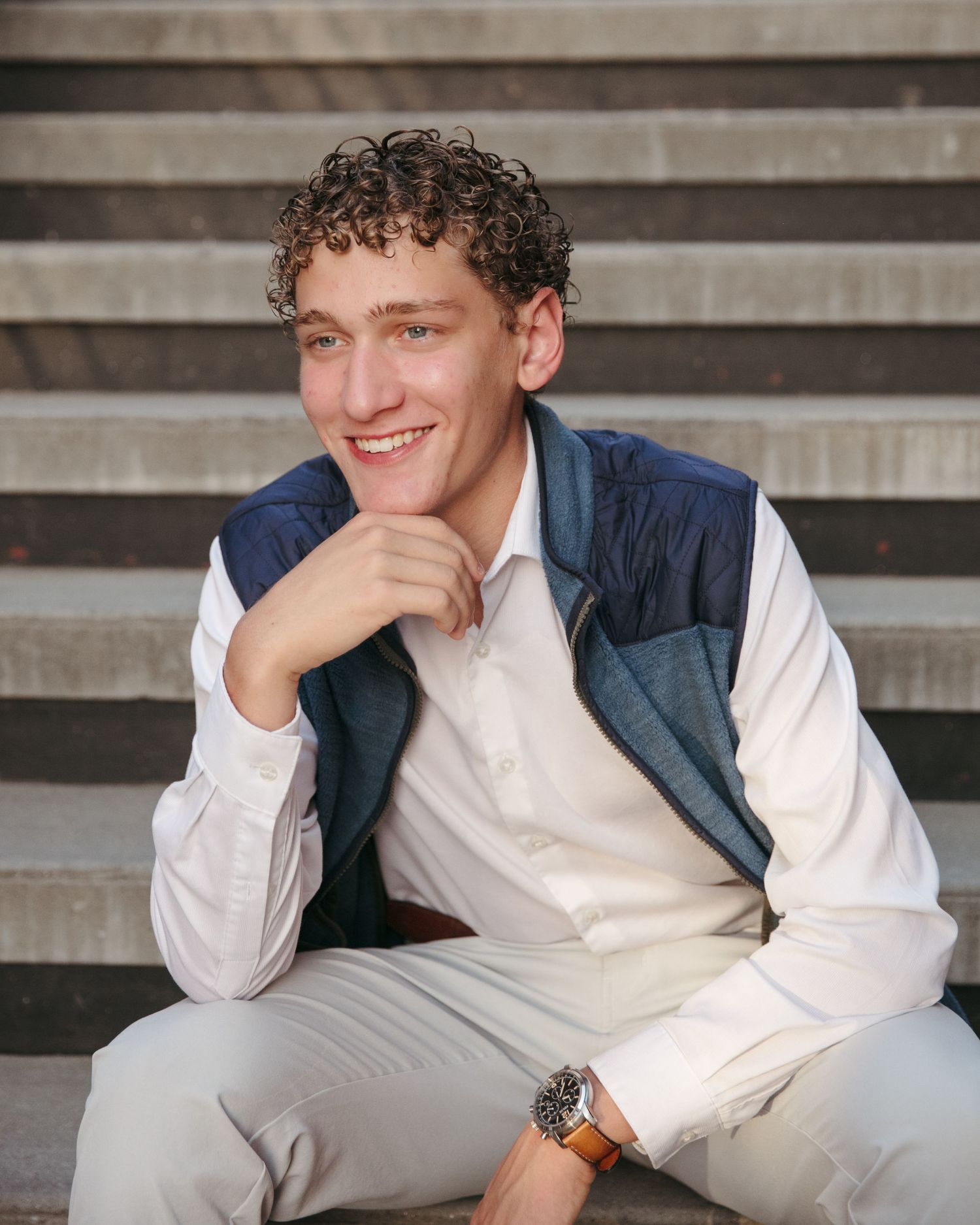 A portrait on concrete stairs featuring someone in casual business wear with a warm expression.