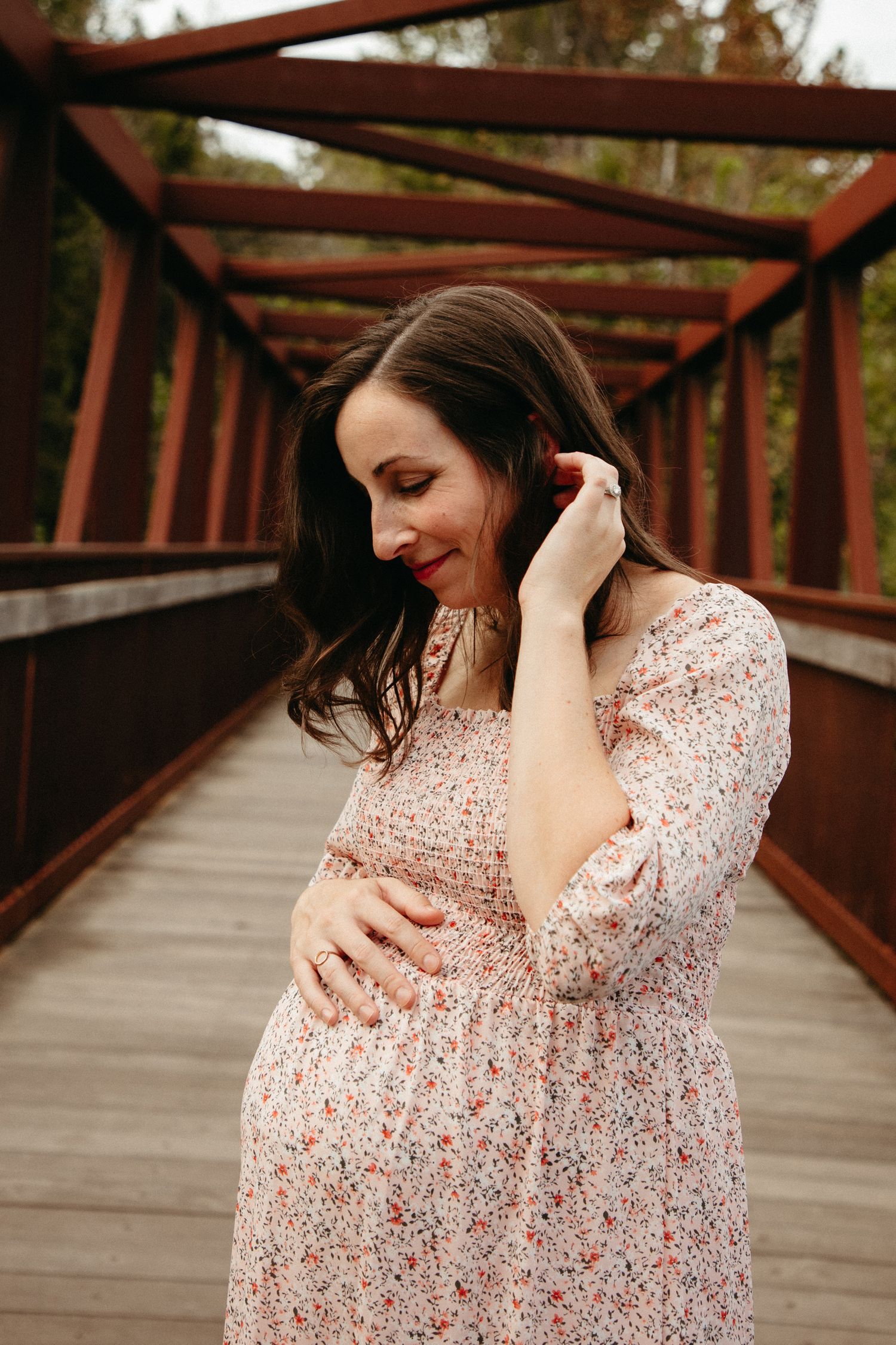 Maternity photo showing a floral dress and gentle hands caressing a baby bump on a wooden bridge.