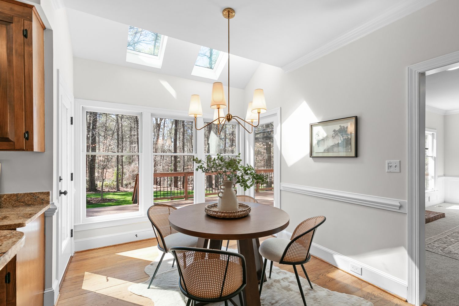 Bright dining nook with skylight, chandelier, round table, French doors, and hardwood floors.