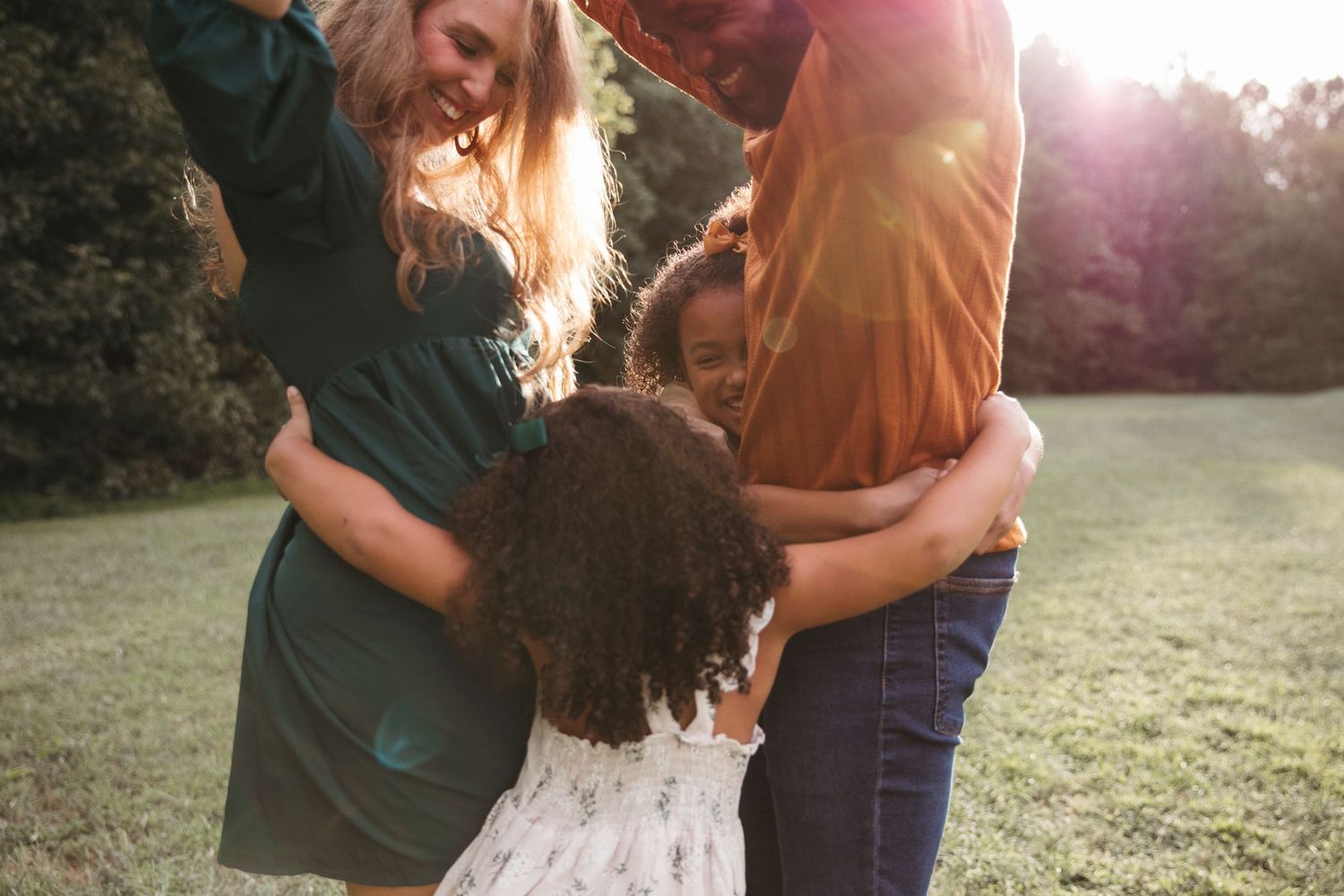 Family embracing in golden sunlight on grassy field during sunset.