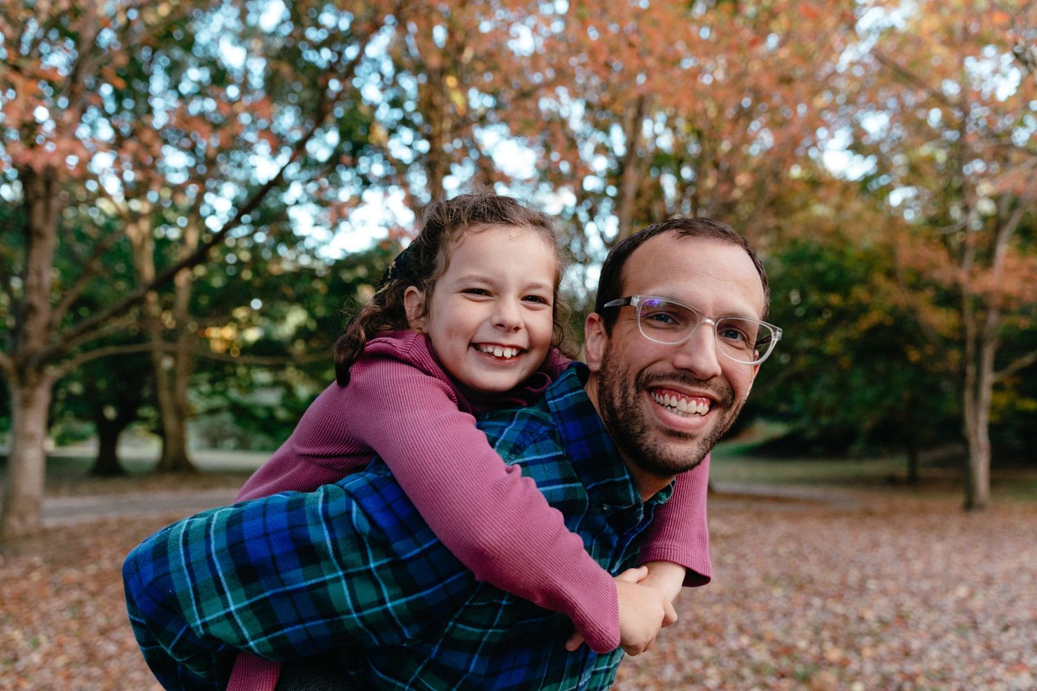 Child and adult sharing a playful piggyback ride in a fall outdoor setting.