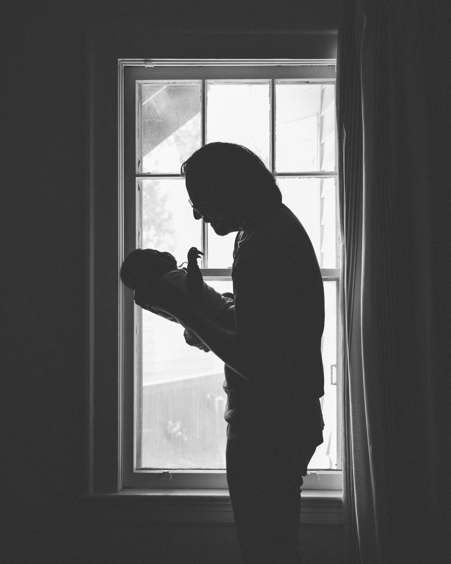 Silhouette against window shows tender moment between parent and infant.