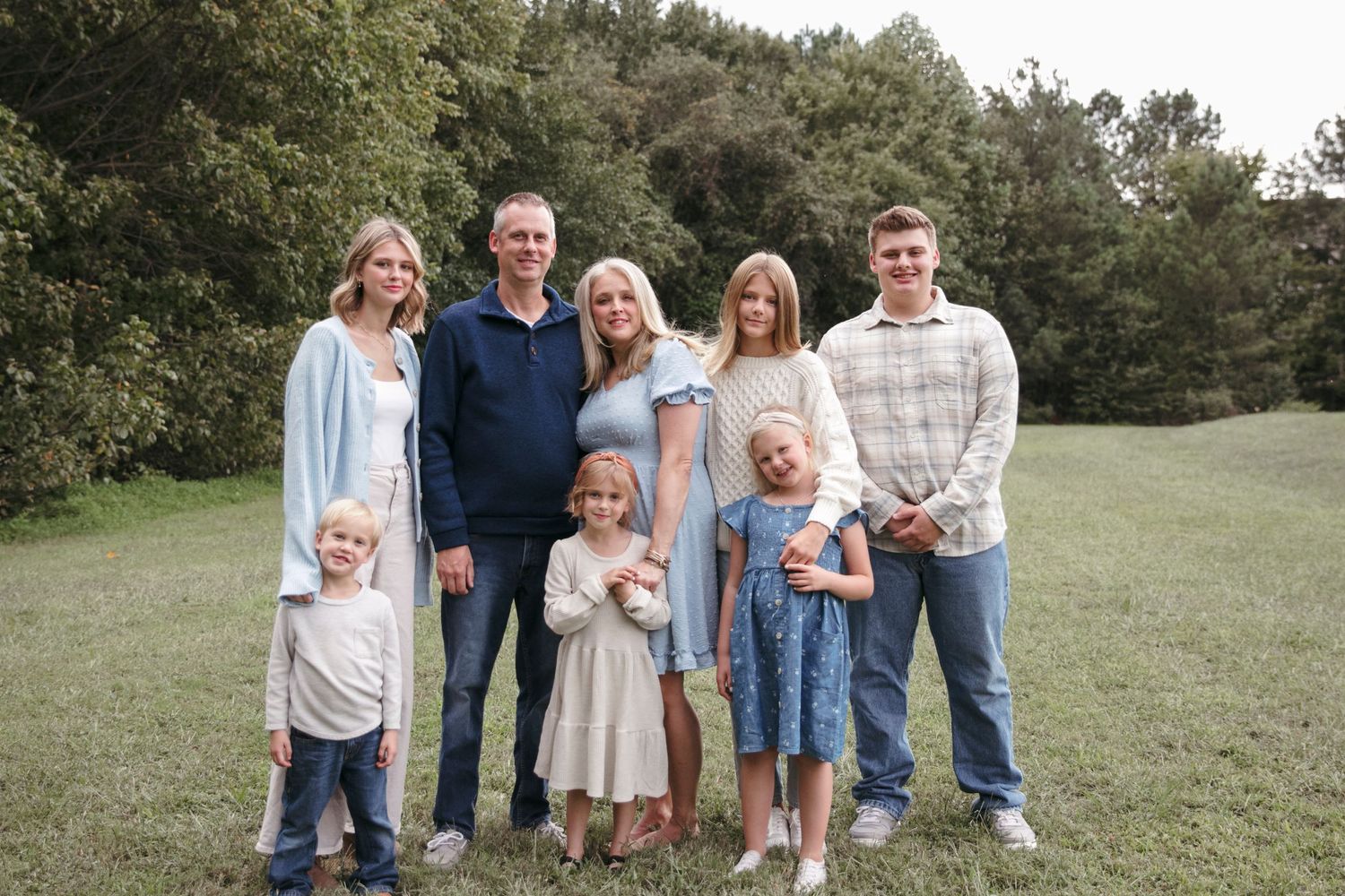 A family poses in casual outfits on a grassy hillside area during an outdoor photo session.
