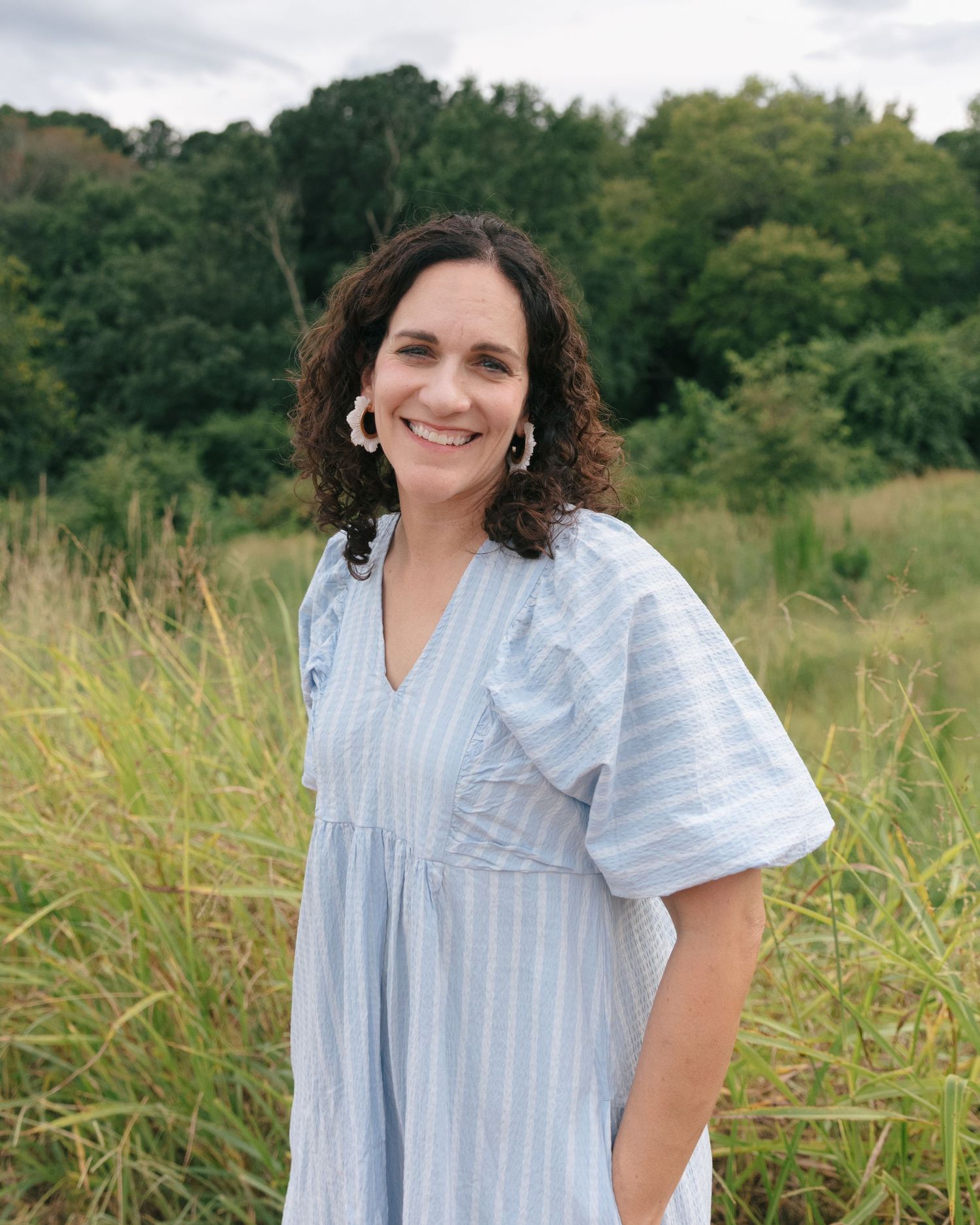 Portrait series in a grassy field featuring a light blue striped summer blouse against green foliage.