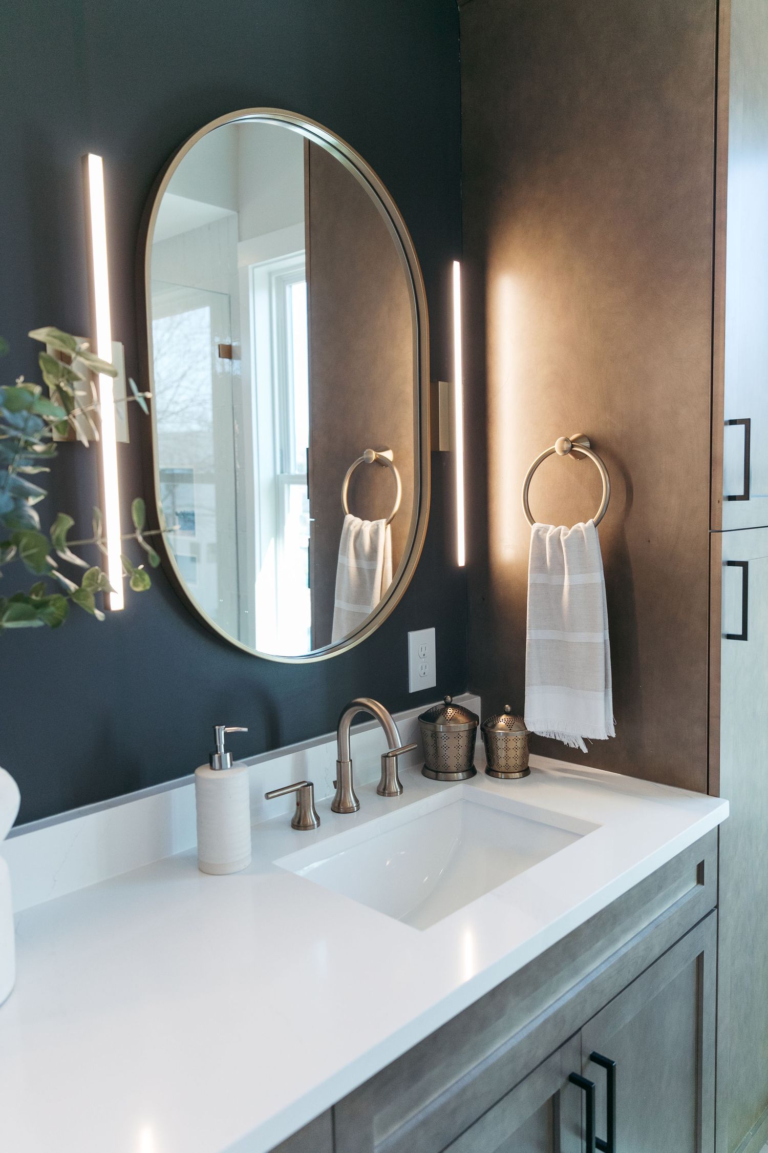 Modern bathroom with dark walls, round mirrors, and white countertops featuring gold fixtures.