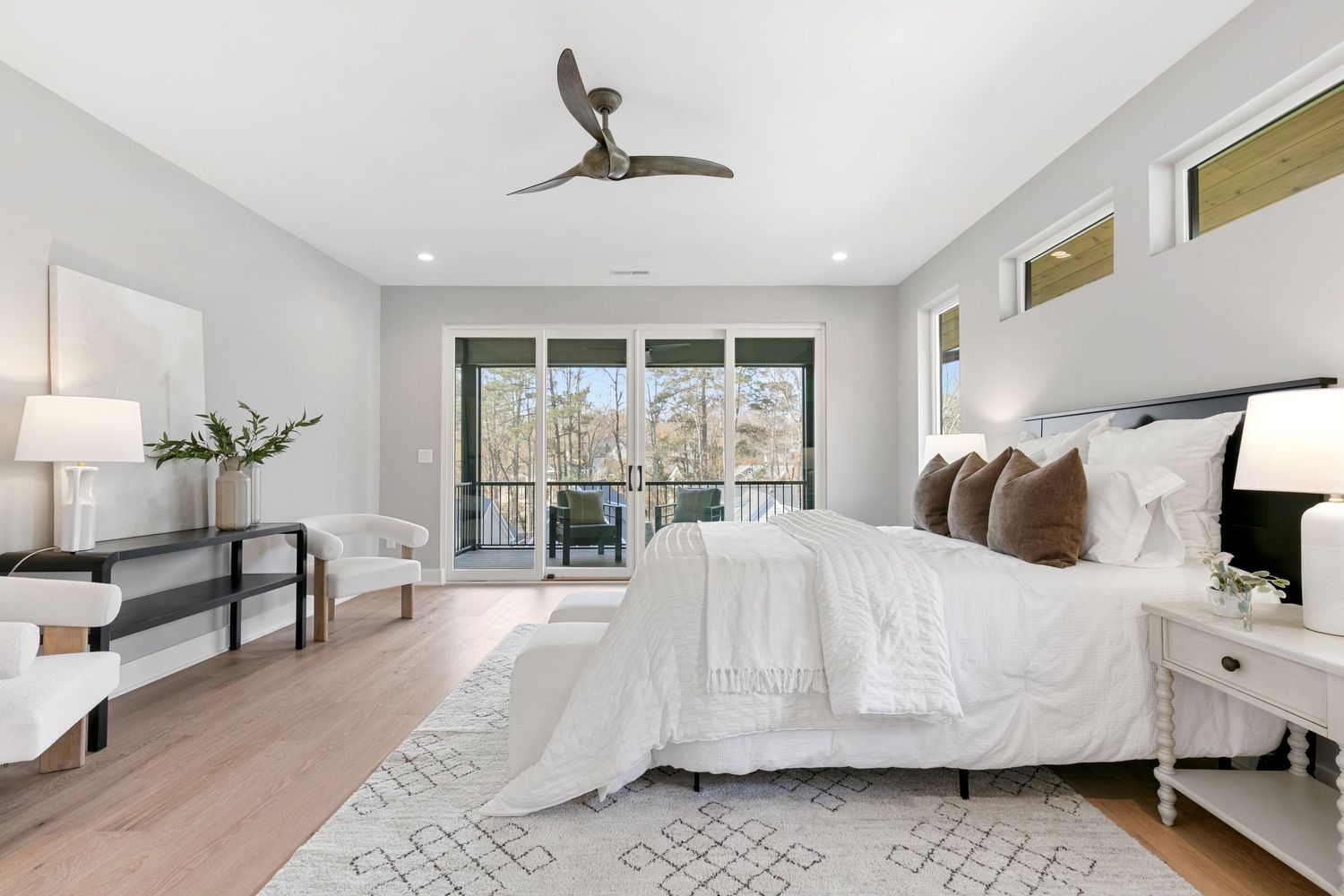 Modern bedroom with white bedding, hardwood floors and sliding glass doors leading to balcony.