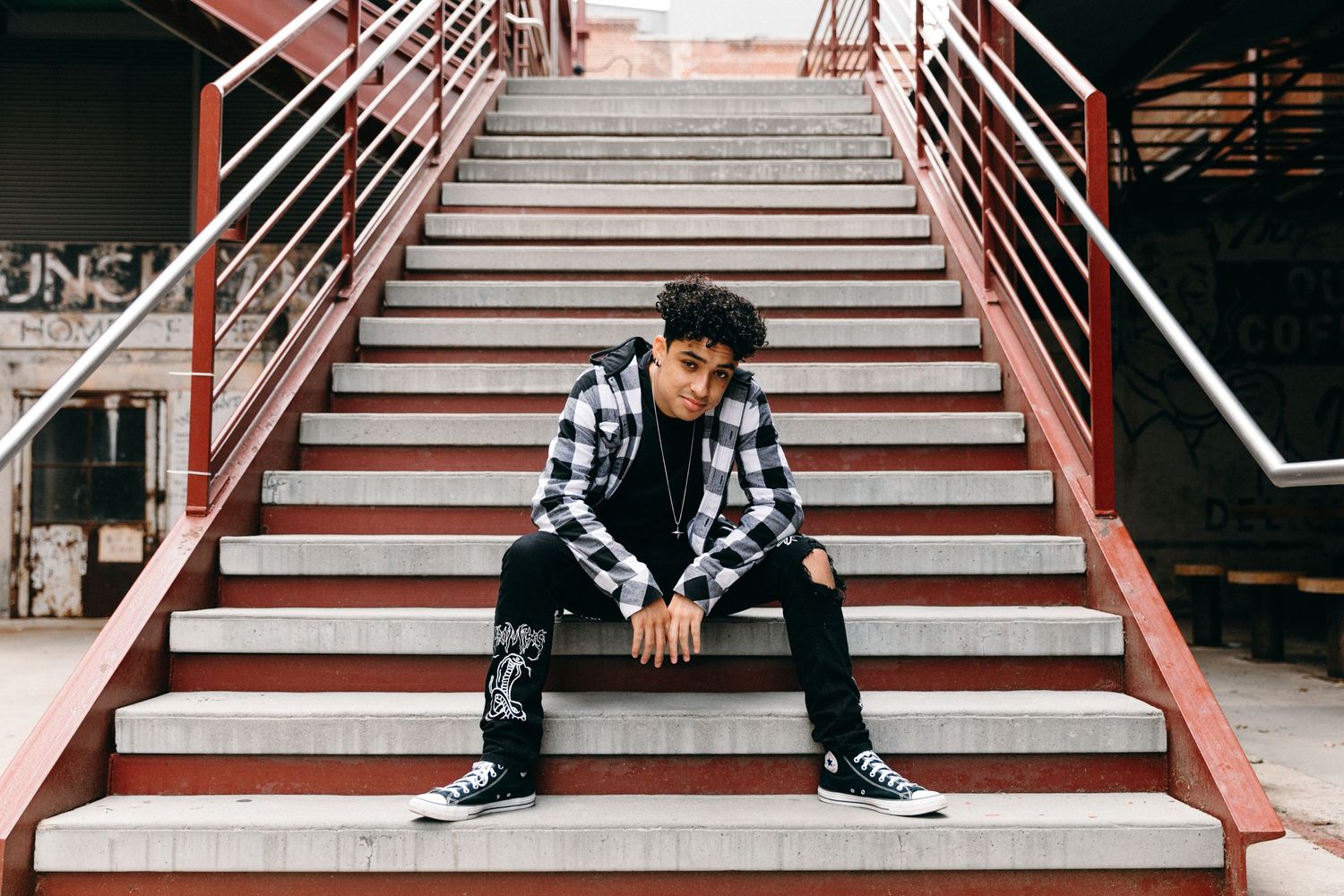 Person in plaid shirt and jeans poses on red metal stairs.