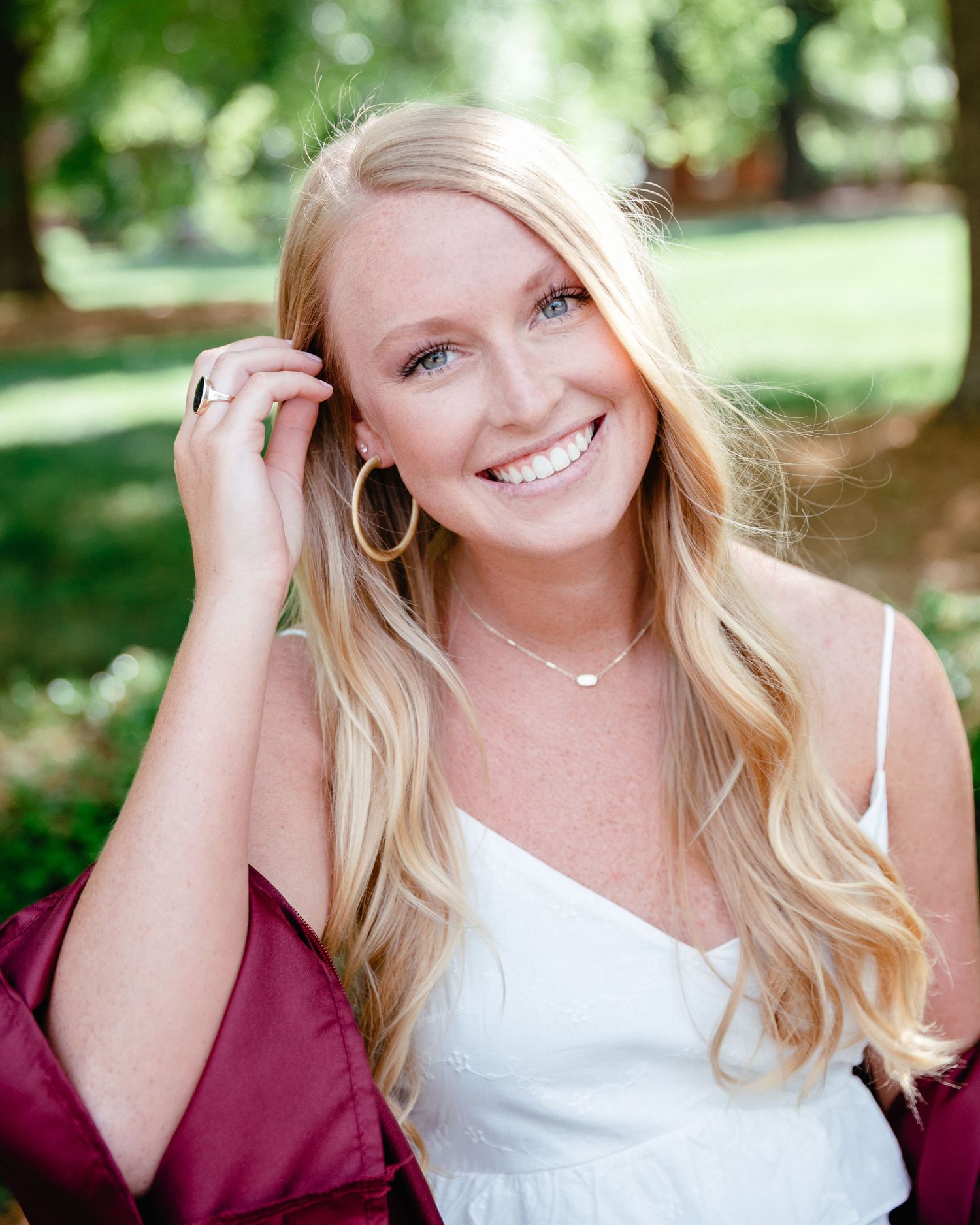 Senior portrait in white top and burgundy graduation gown outdoors.