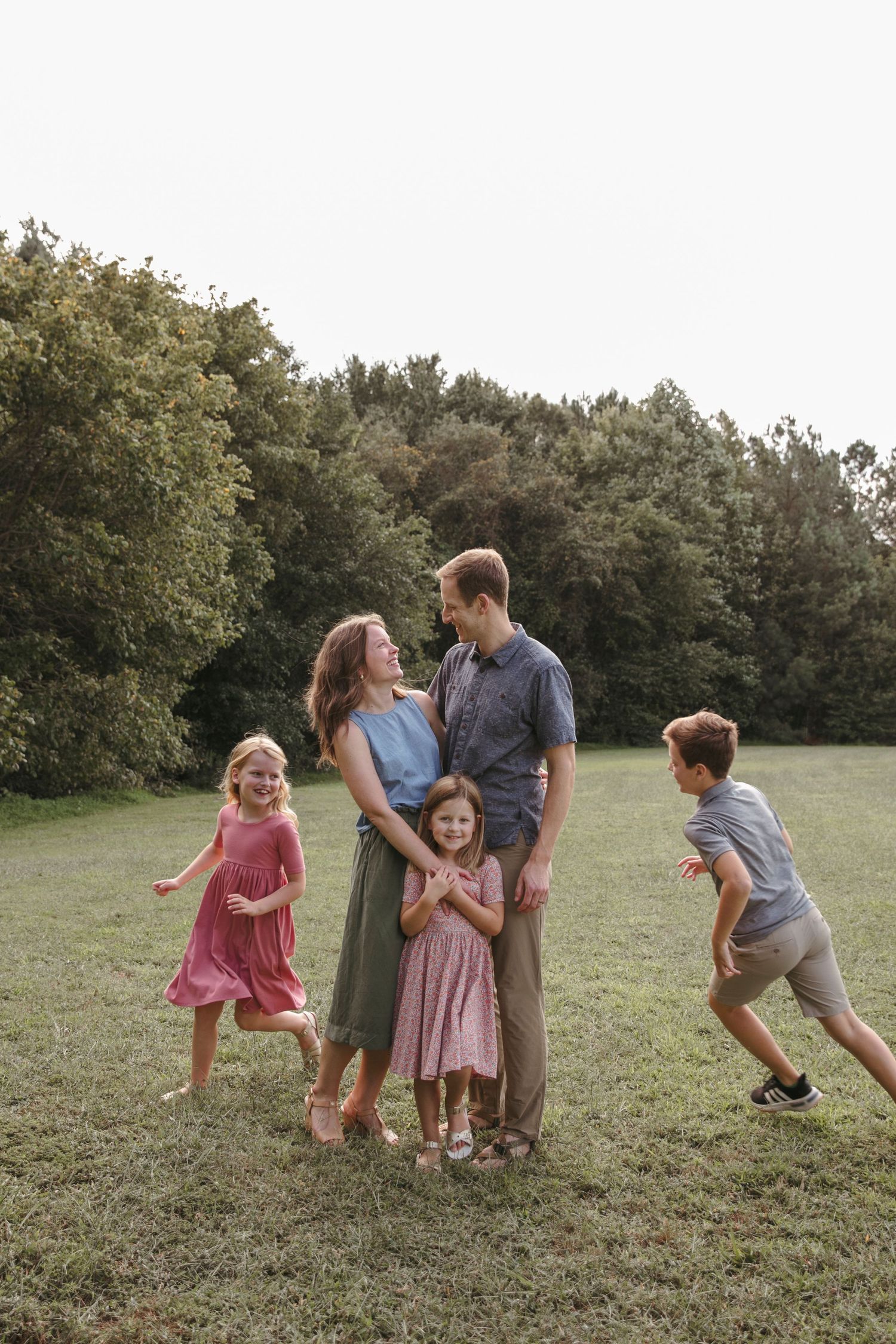 A fun family portrait taken outdoors with children playing and running in a grassy field.
