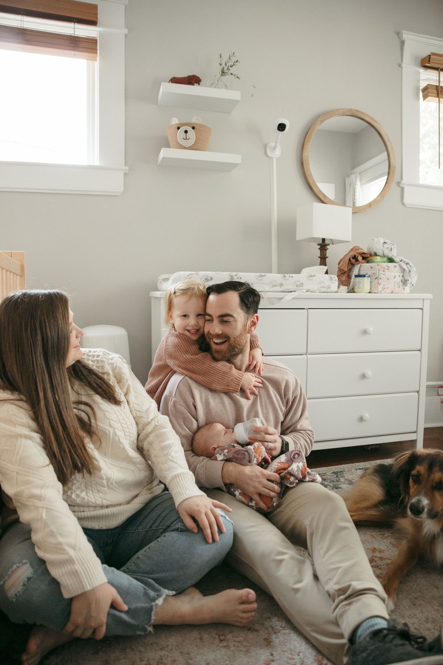 Cozy nursery scene with white dresser, round mirror, and decorative shelving.