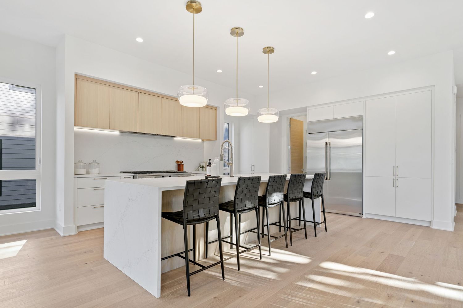 Contemporary white kitchen with island seating, pendant lights, and light wood accents.