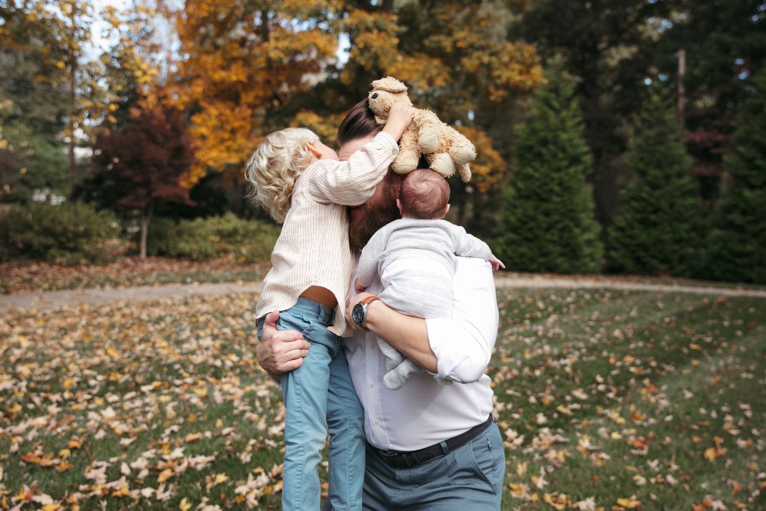 A couple shares tender moments in a fall setting with autumn leaves scattered on the ground and trees in the background.