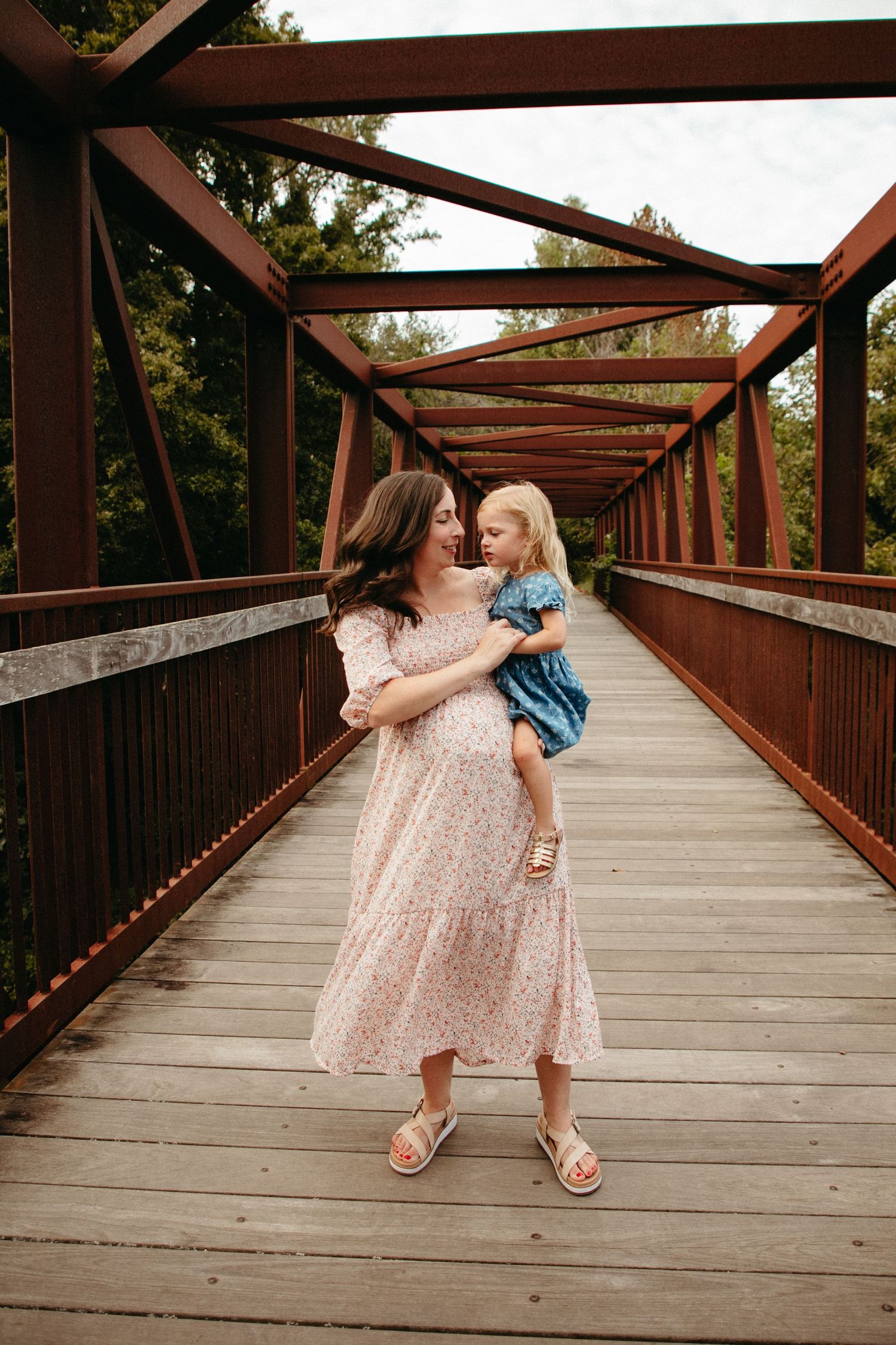 A tender moment between parent and child on a rustic wooden bridge with metal beams.