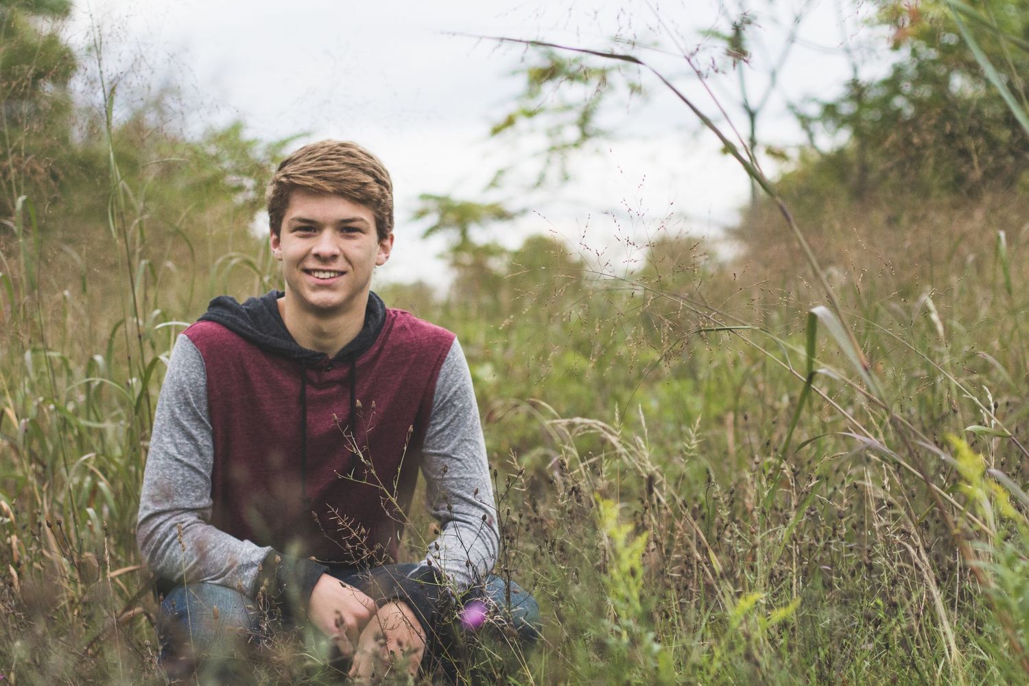 Portrait in a natural outdoor setting with greenery and trees in the background.