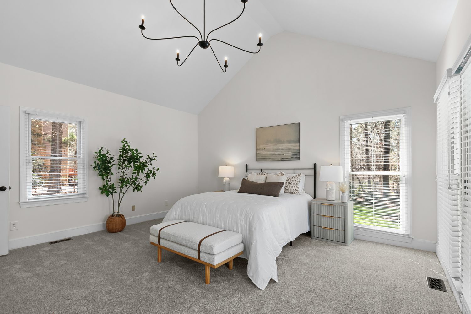 Bright master bedroom with vaulted ceilings, modern chandelier, plush carpet, and large windows flooding natural light.